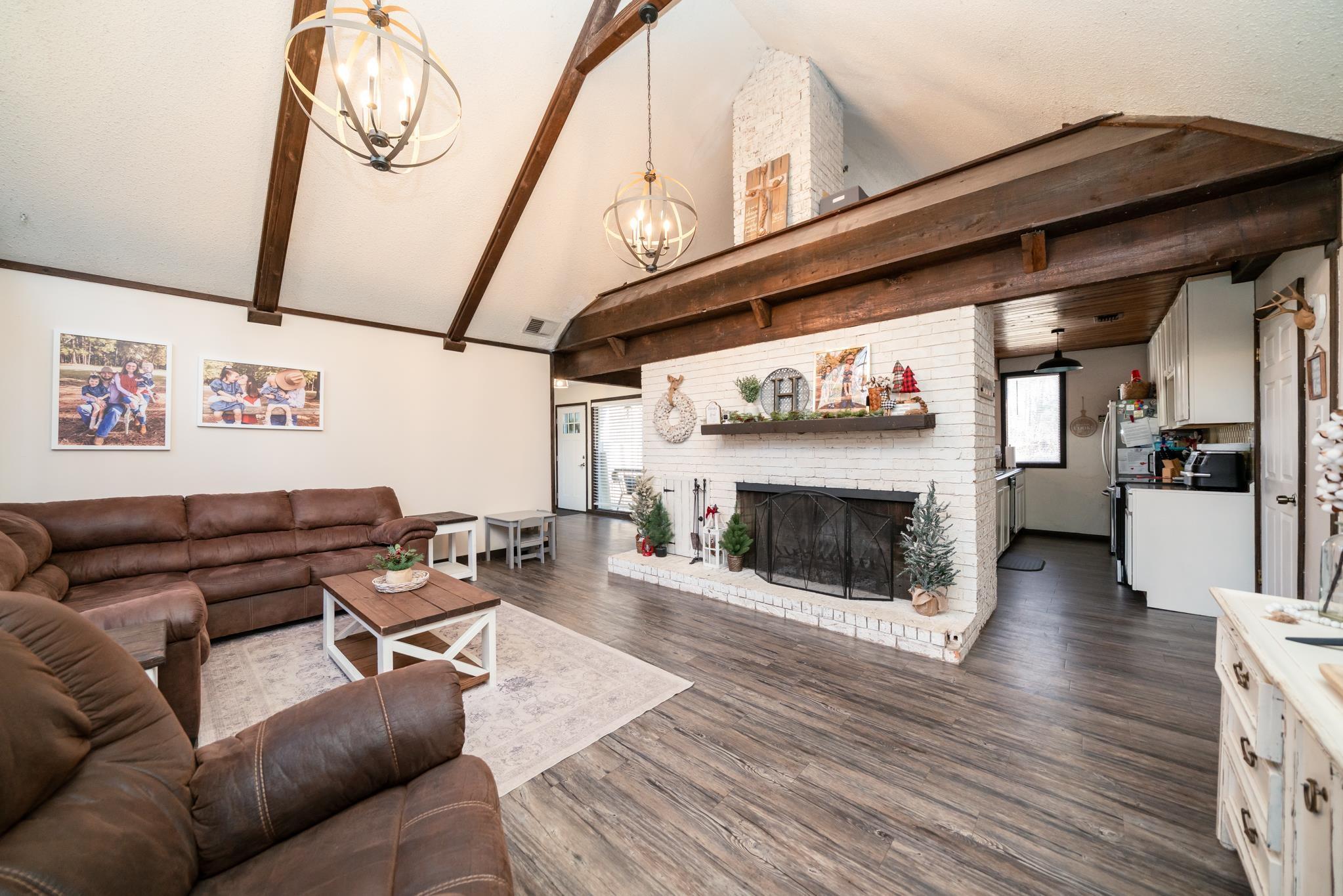 Image 3: Living room with lofted ceiling, dark wood-style floors, a chandelier, a brick fireplace, and healthy amount of natural light, Living Room