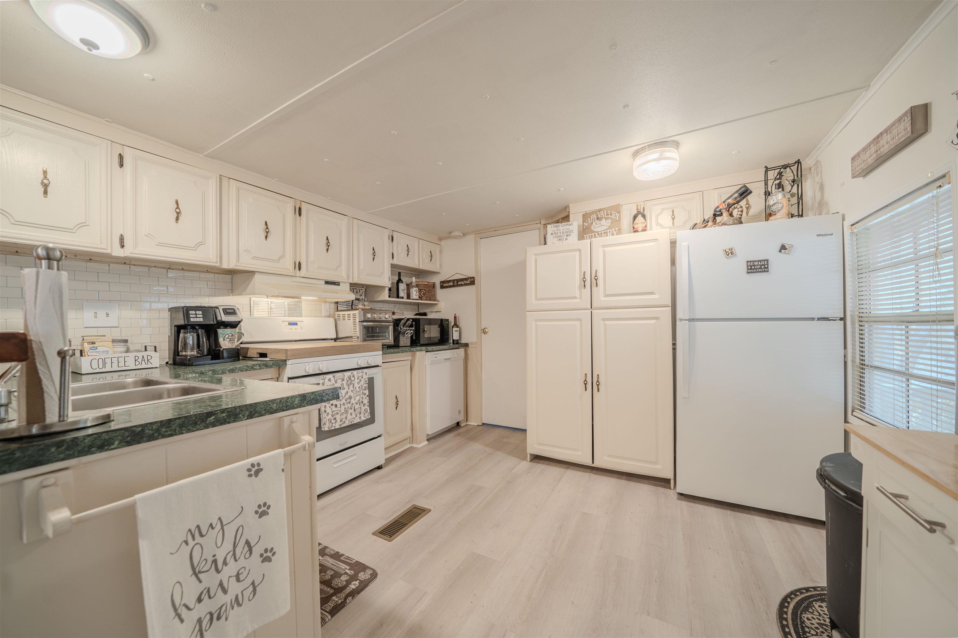 Image 3: Kitchen featuring white appliances, white cabinets, dark countertops, backsplash, and light wood-type flooring, Kitchen