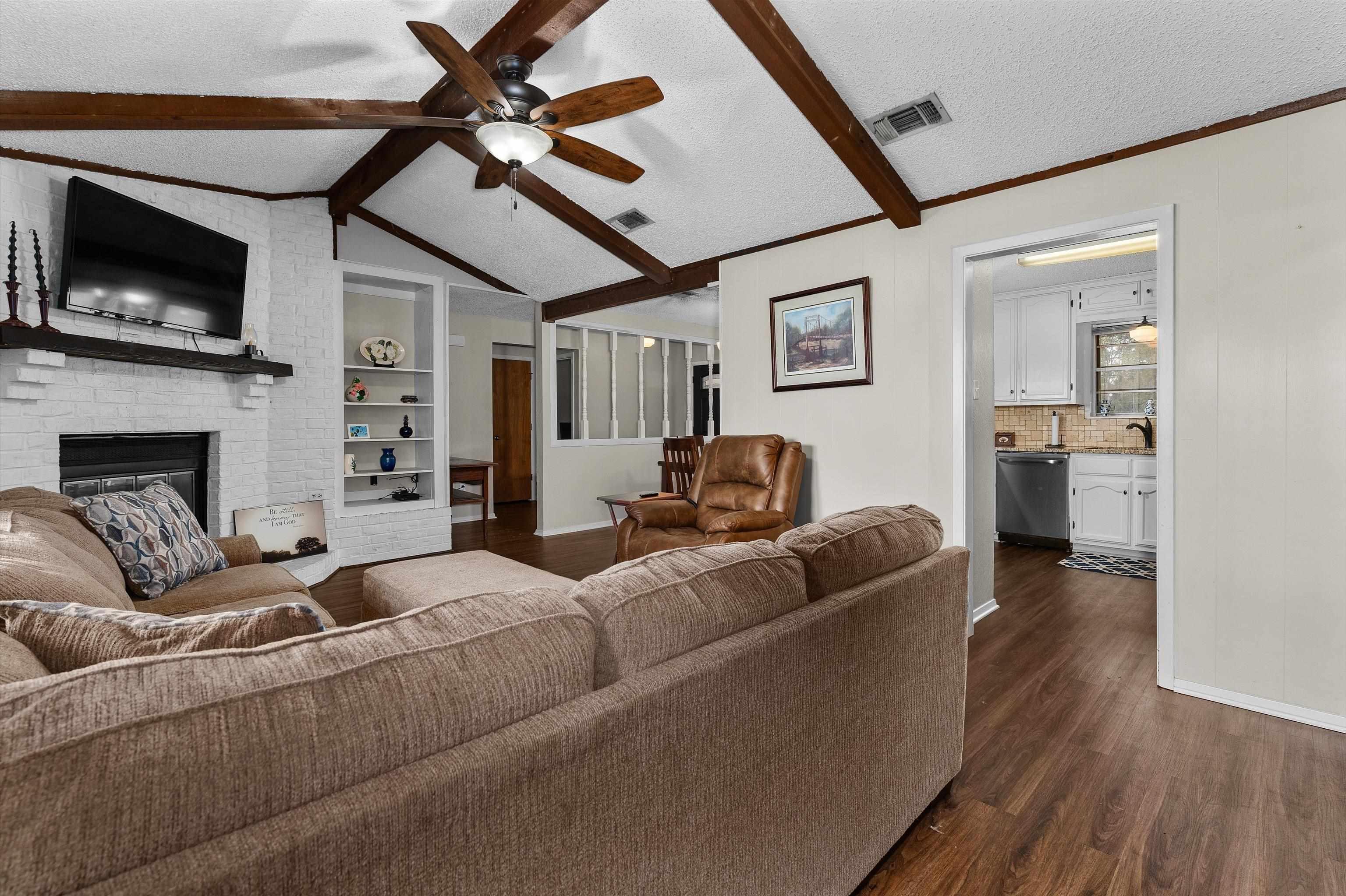 Image 1: Living room with a textured ceiling, dark wood finished floors, a brick fireplace, a ceiling fan, and built in shelves, Living Room