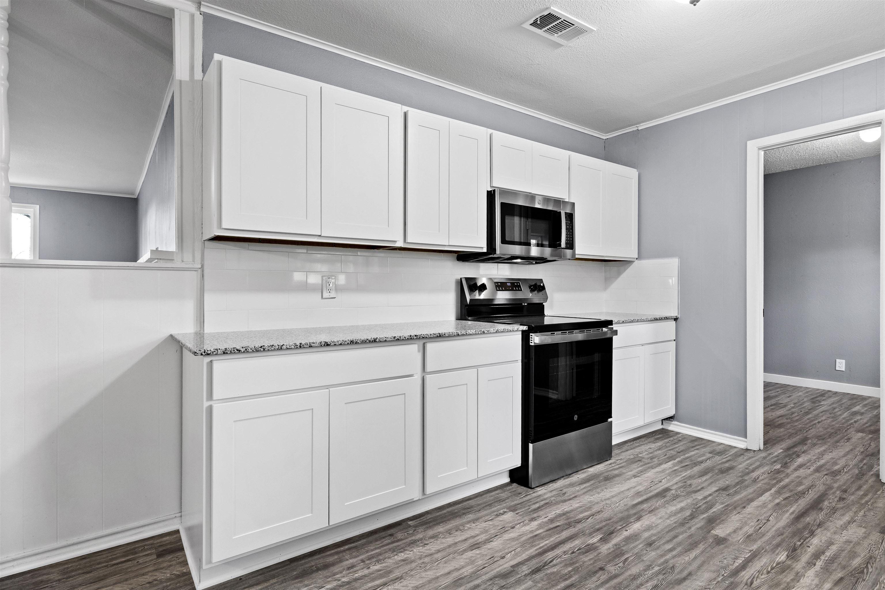 Image 2: Kitchen featuring stainless steel appliances, white cabinetry, light stone counters, dark wood finished floors, and a textured ceiling, Kitchen