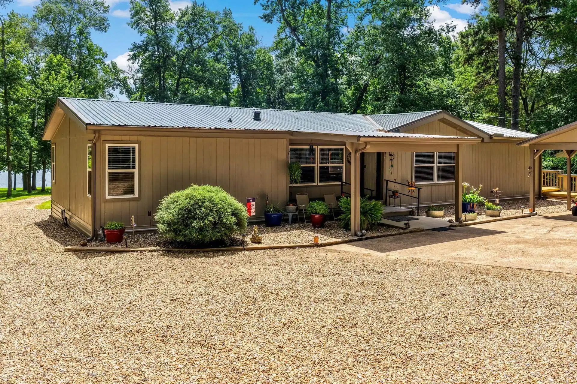 Image 0: Exterior featuring a corrugated metal roof, covered entry with handrails, gravel driveway, and surrounding mature trees, Front Of Structure