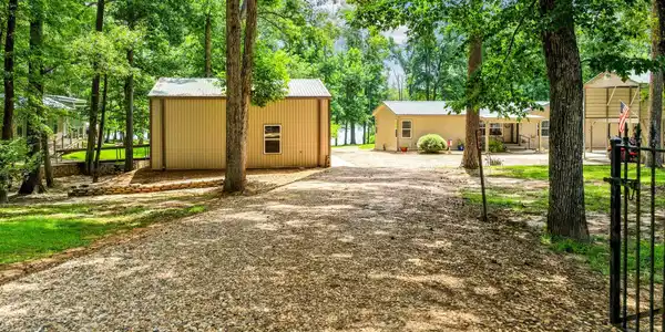Image 3: Gravel driveway leading to two structures, surrounded by mature trees, Front Of Structure