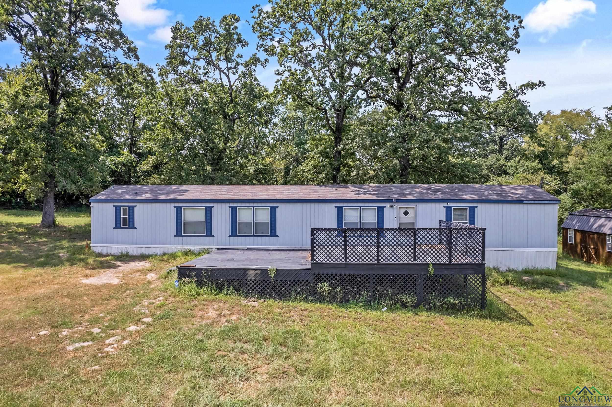 Image 1: Back of property featuring a lawn, a wooden deck, and view of scattered trees, Back Of Structure