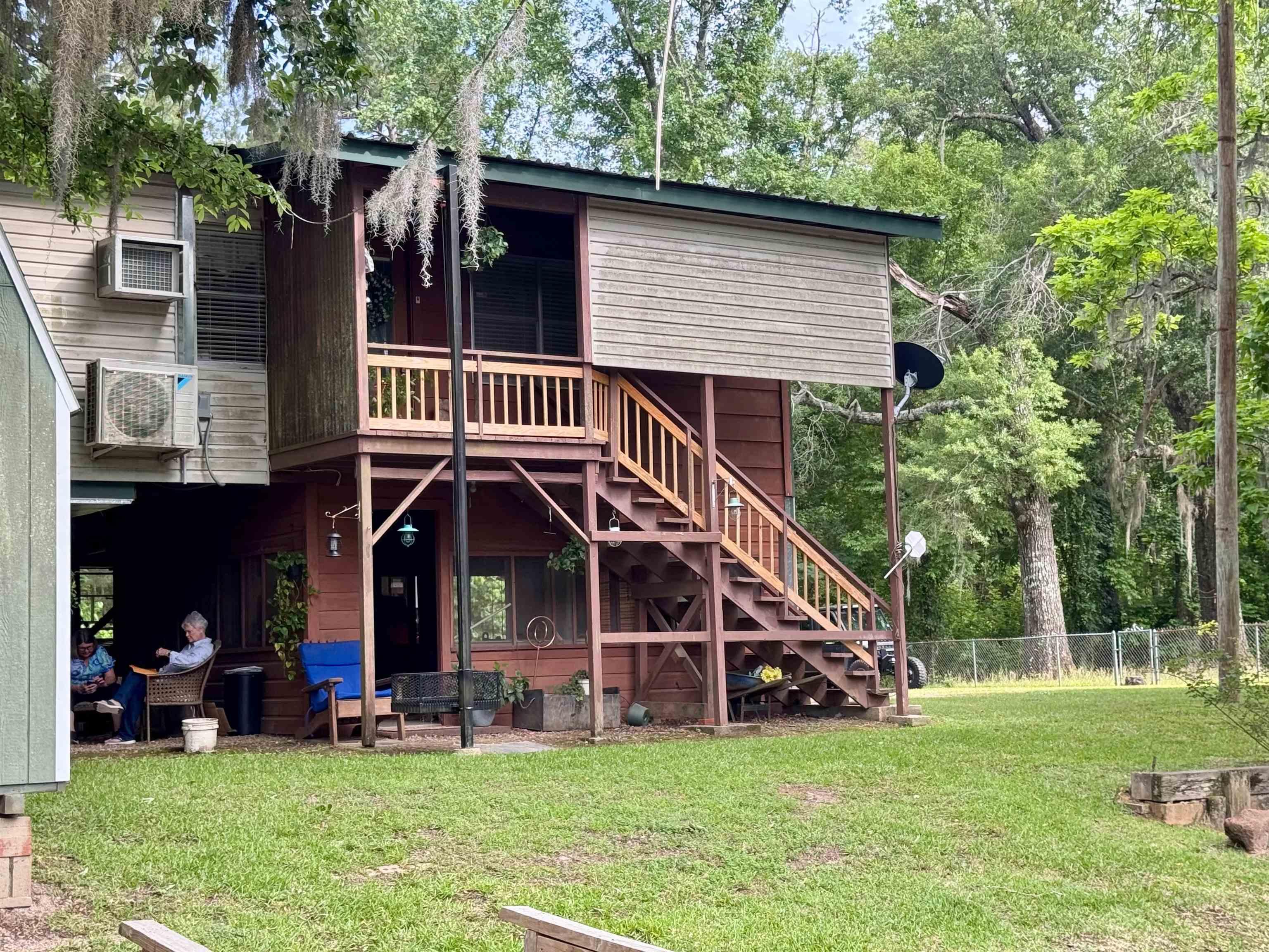 Image 2: Two-story residential structure featuring a screened upper balcony, exterior staircase, lower covered patio, and a metal roof, Back Of Structure