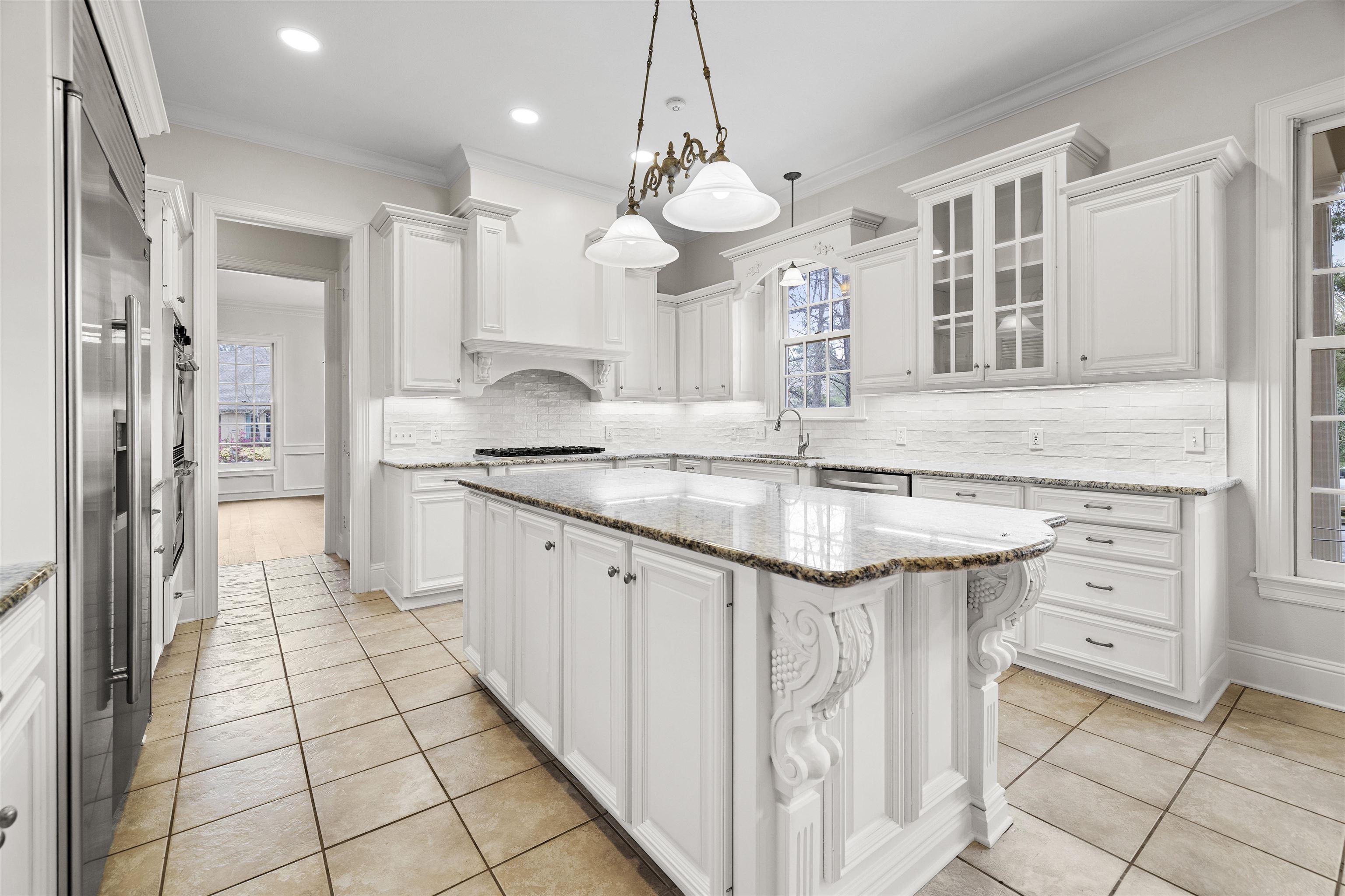 Image 2: Kitchen with light stone countertops, crown molding, a center island, glass insert cabinets, and white cabinetry, Kitchen