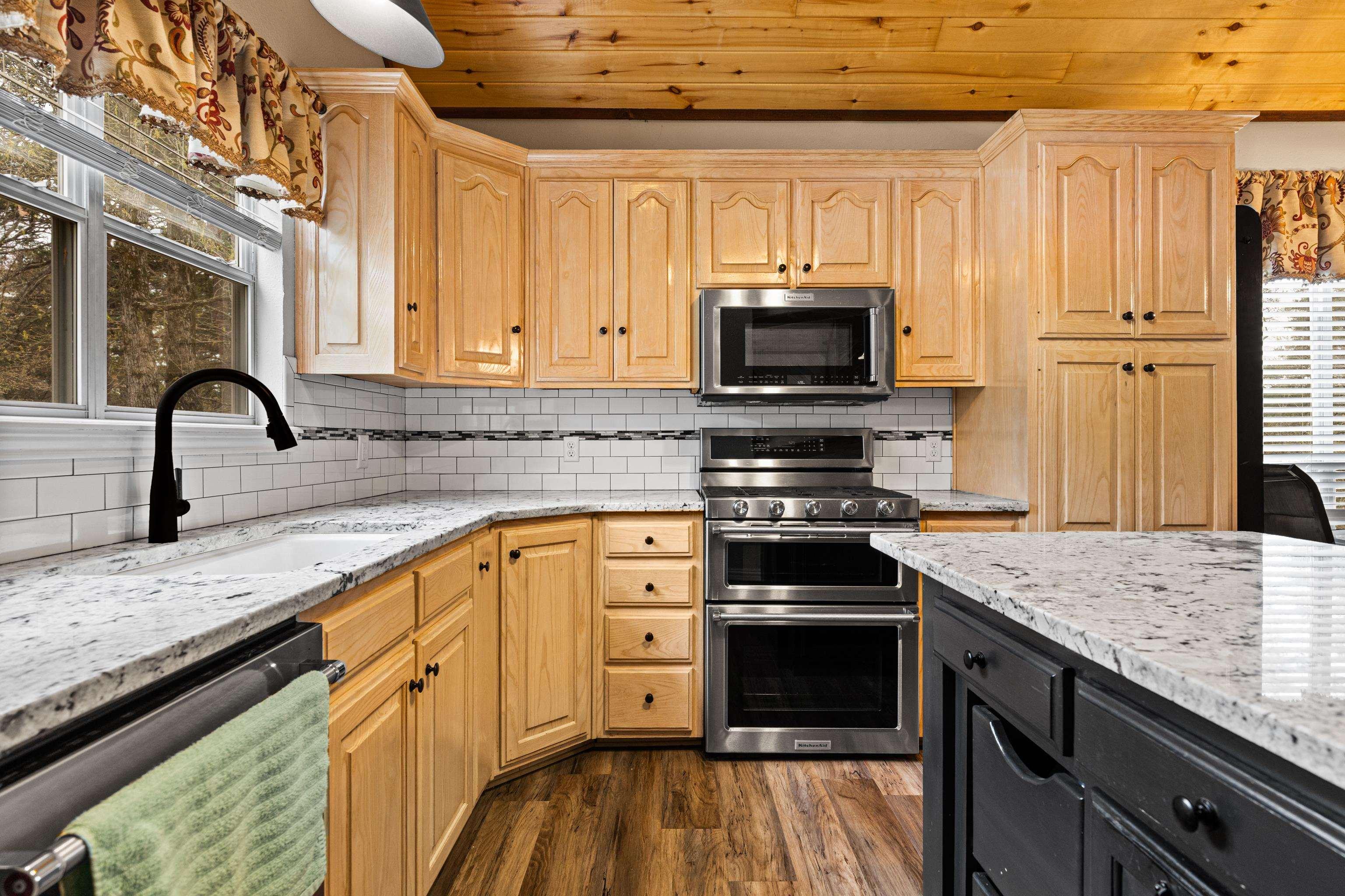 Image 2: Two tone kitchen featuring light stone counters, stainless steel appliances, dual tone cabinets, and dark wood finished floors, Kitchen