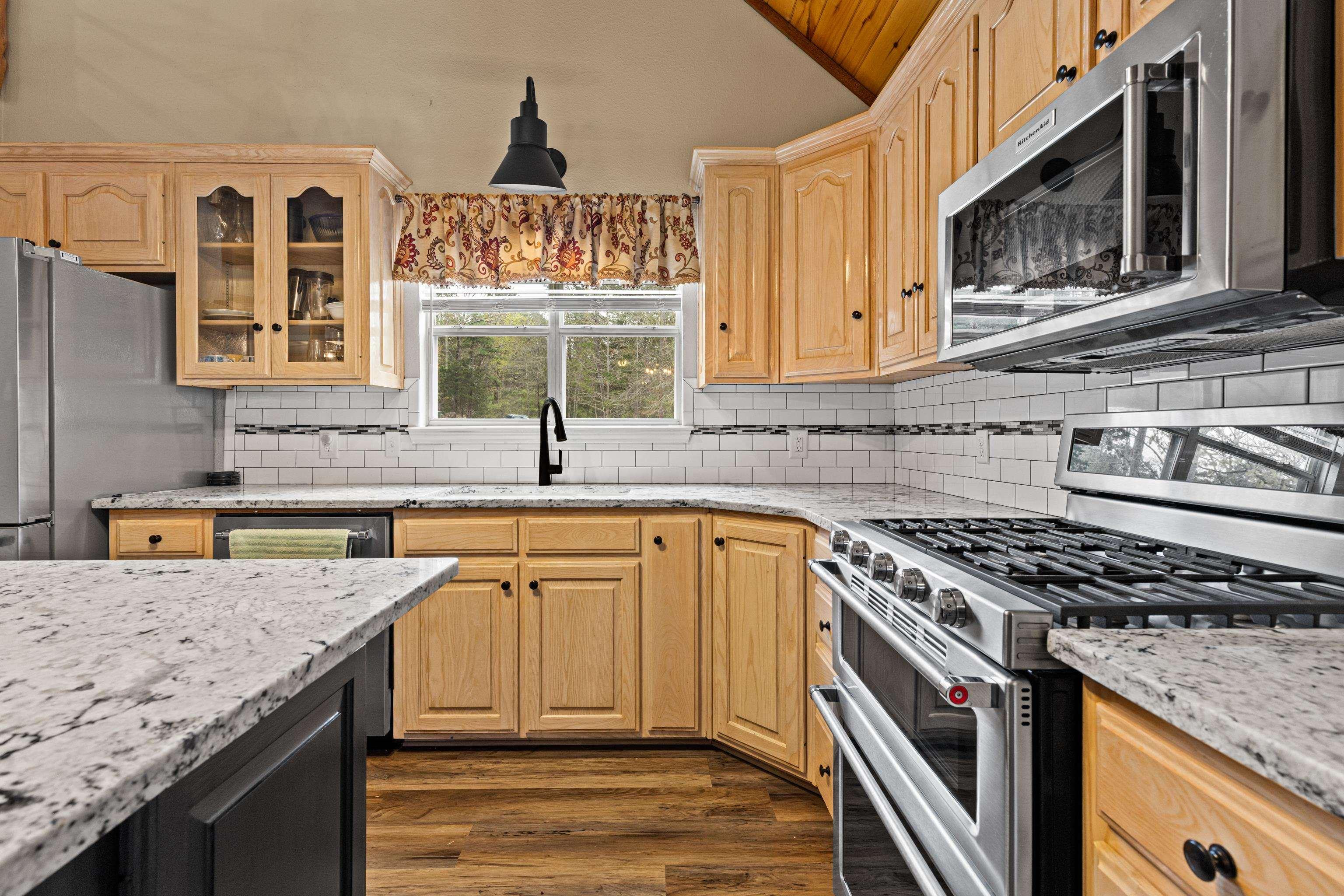 Image 3: Dual tone kitchen with stainless steel appliances, light stone counters, glass insert cabinets, vaulted ceiling, and two tone cabinetry, Kitchen