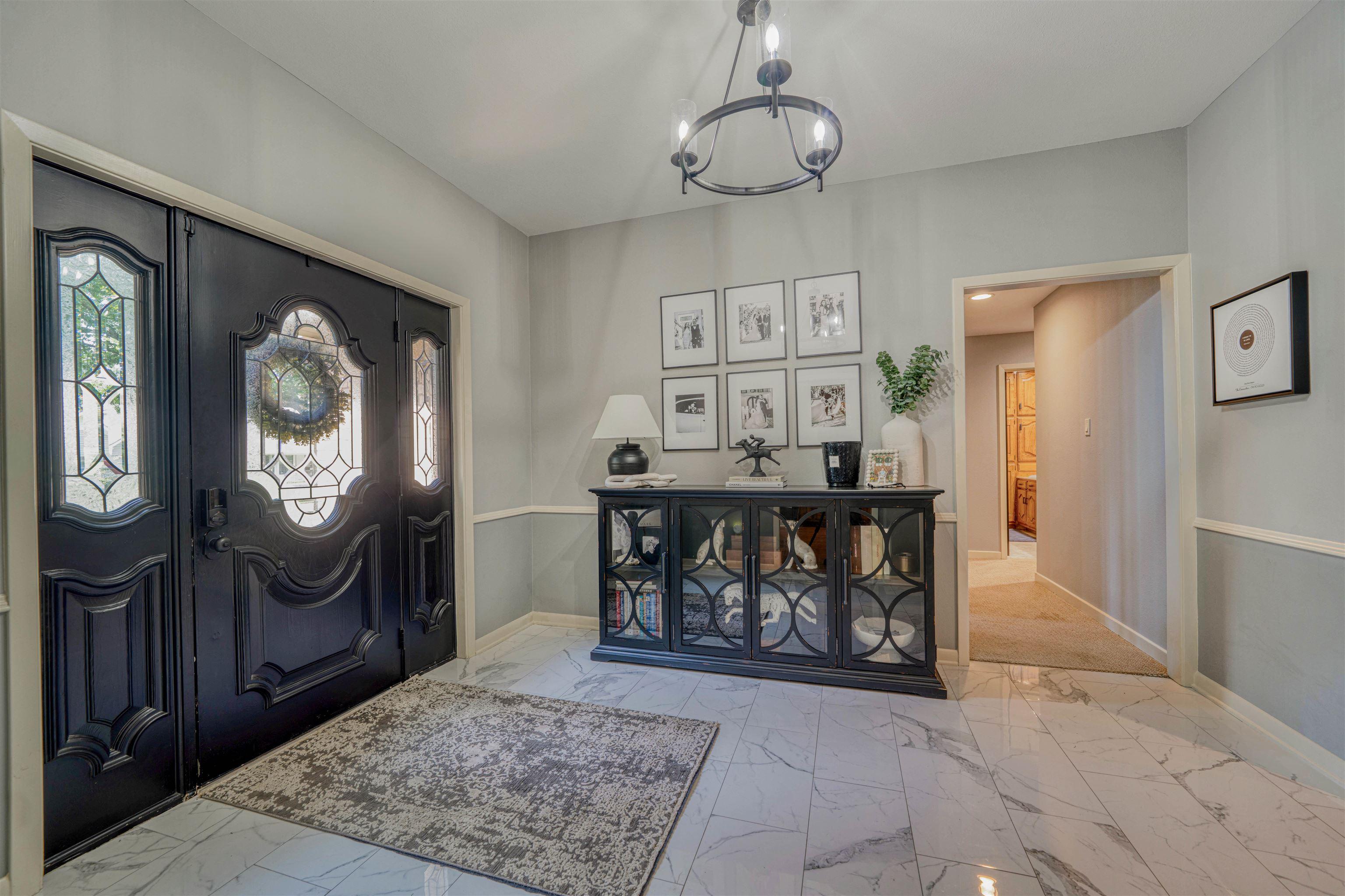 Image 3: Foyer featuring double entry doors with decorative glass inserts and sidelights, marble-look tile flooring, wainscoting, and an overhead chandelier, Entrance Foyer