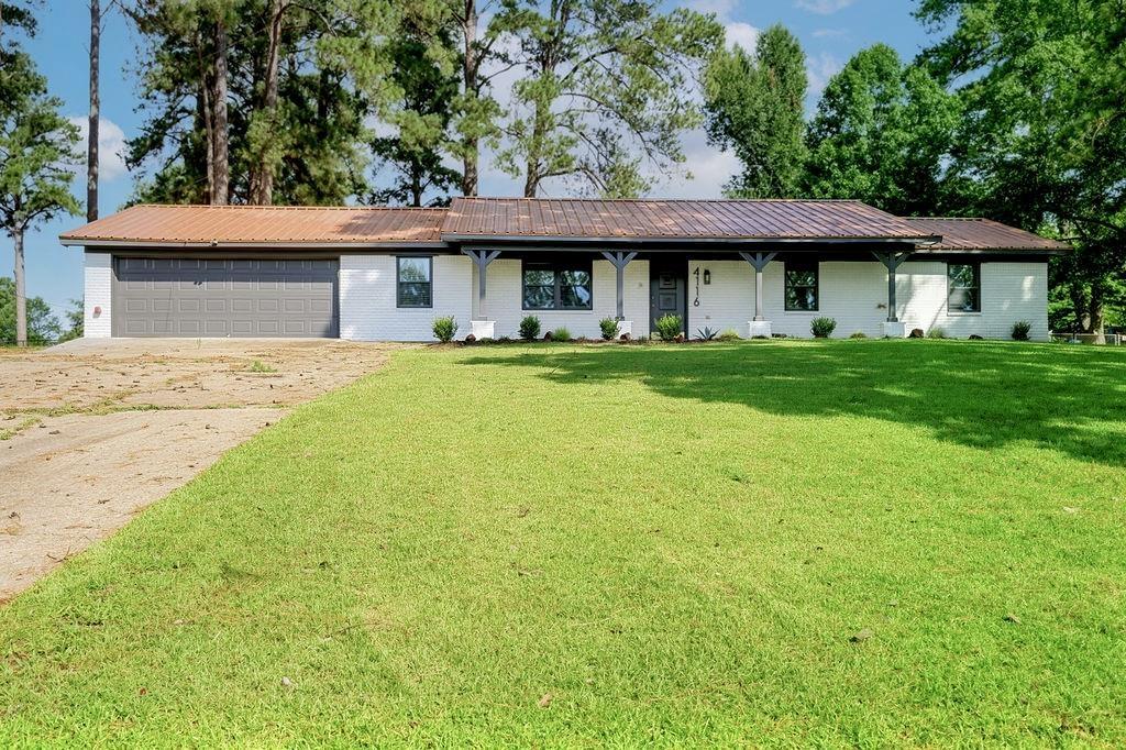 Image 2: White brick exterior featuring a metal roof, attached garage, covered front porch with dark wood posts, and dark-framed windows, Front Of Structure