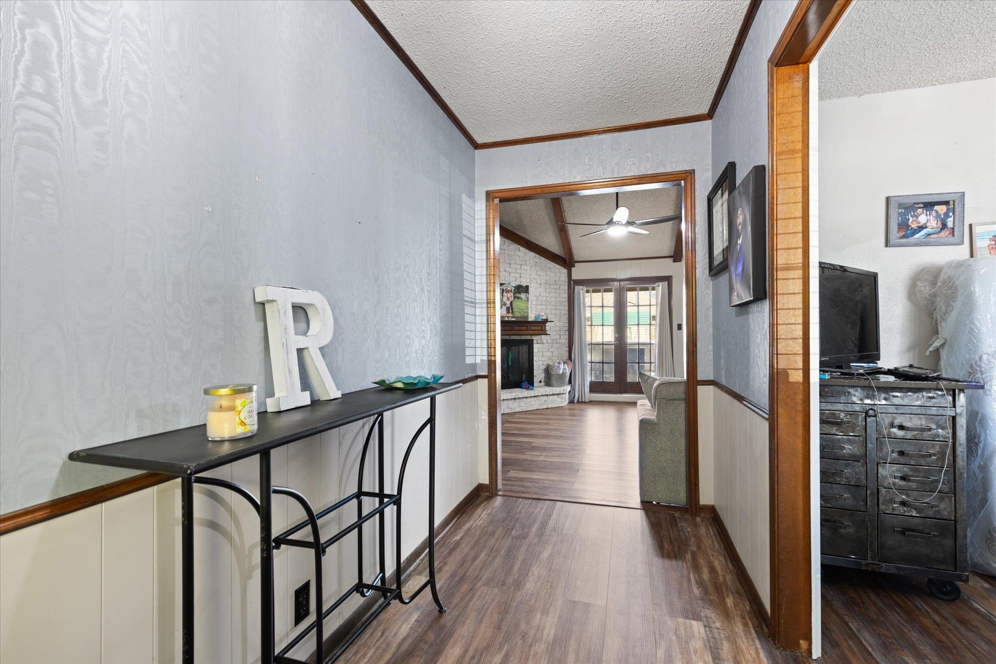 Image 3: Hall with crown molding, a textured ceiling, dark wood-style floors, a wainscoted wall, and a textured wall, Hallway