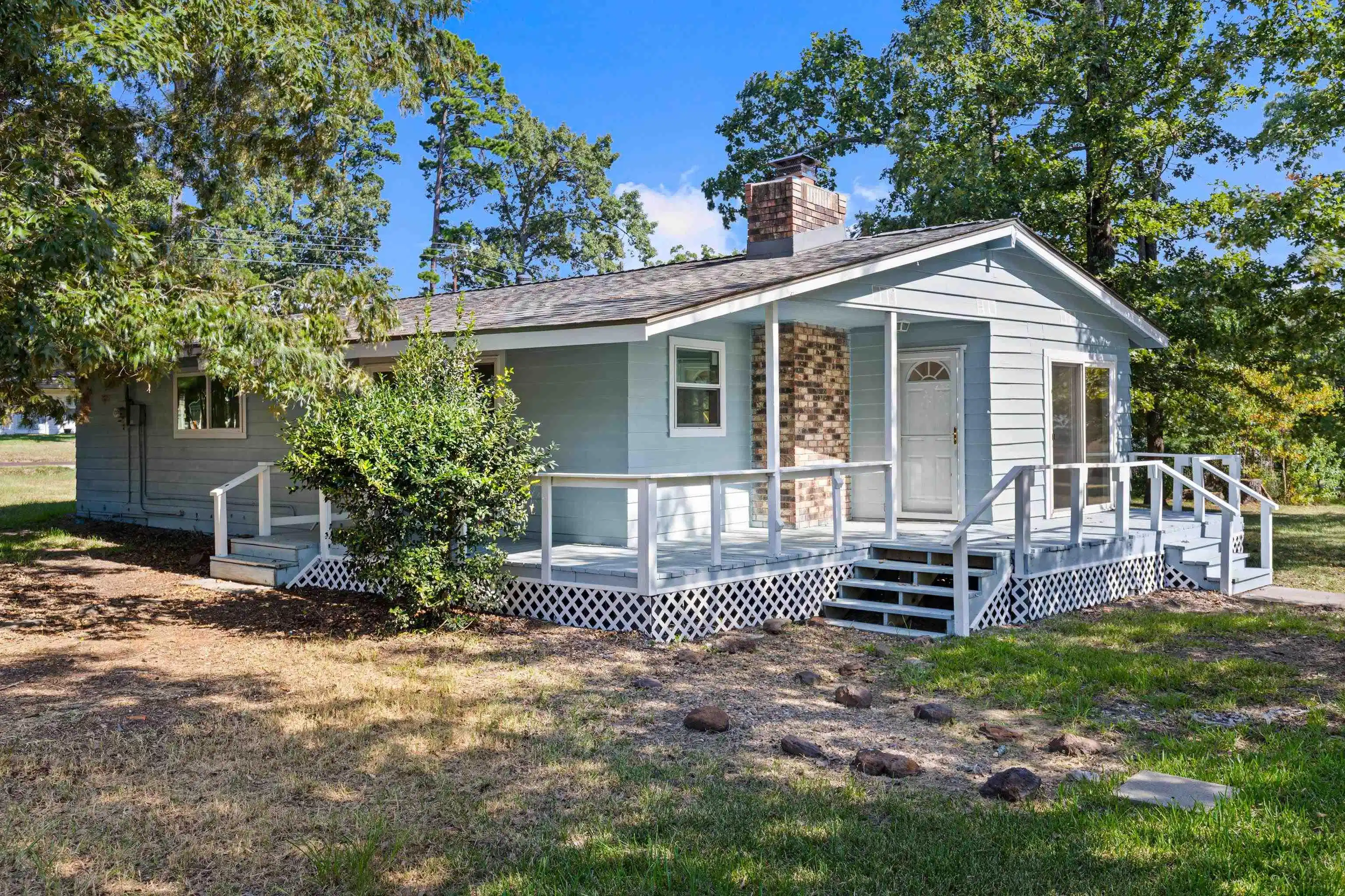 Image 0: Light blue siding exterior with a wraparound porch featuring white railings and lattice skirting, Front Of Structure