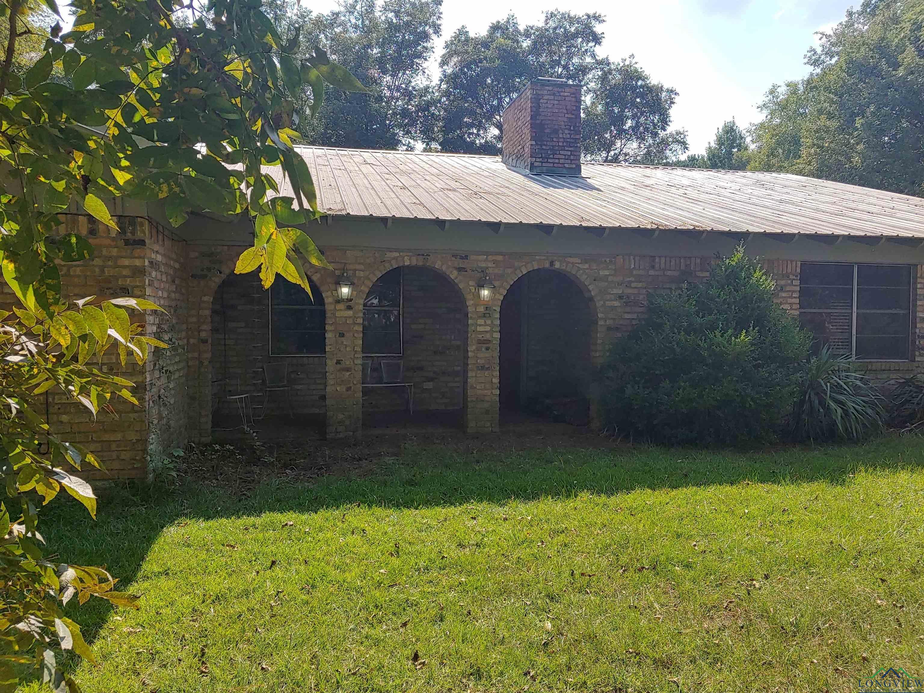 Image 0: Front of the house with brick exterior, triple arch front architecture at the entrance.  Front yard & metal roof., Front Of Structure