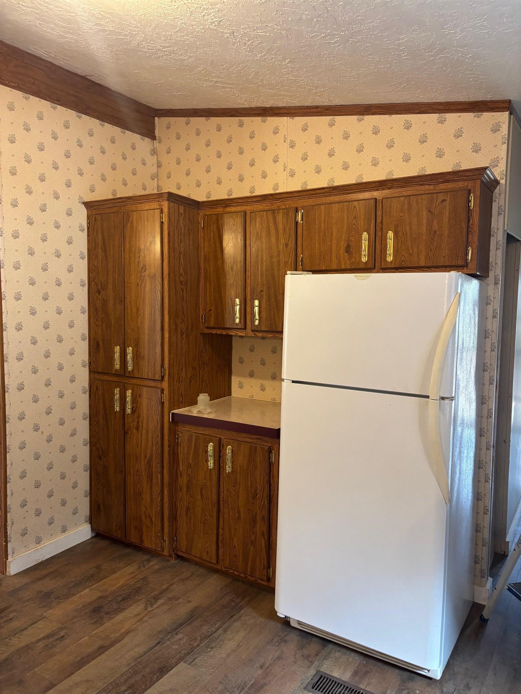 Image 3: Kitchen with freestanding refrigerator, wallpapered walls, dark wood-style flooring, light countertops, and a textured ceiling, Kitchen