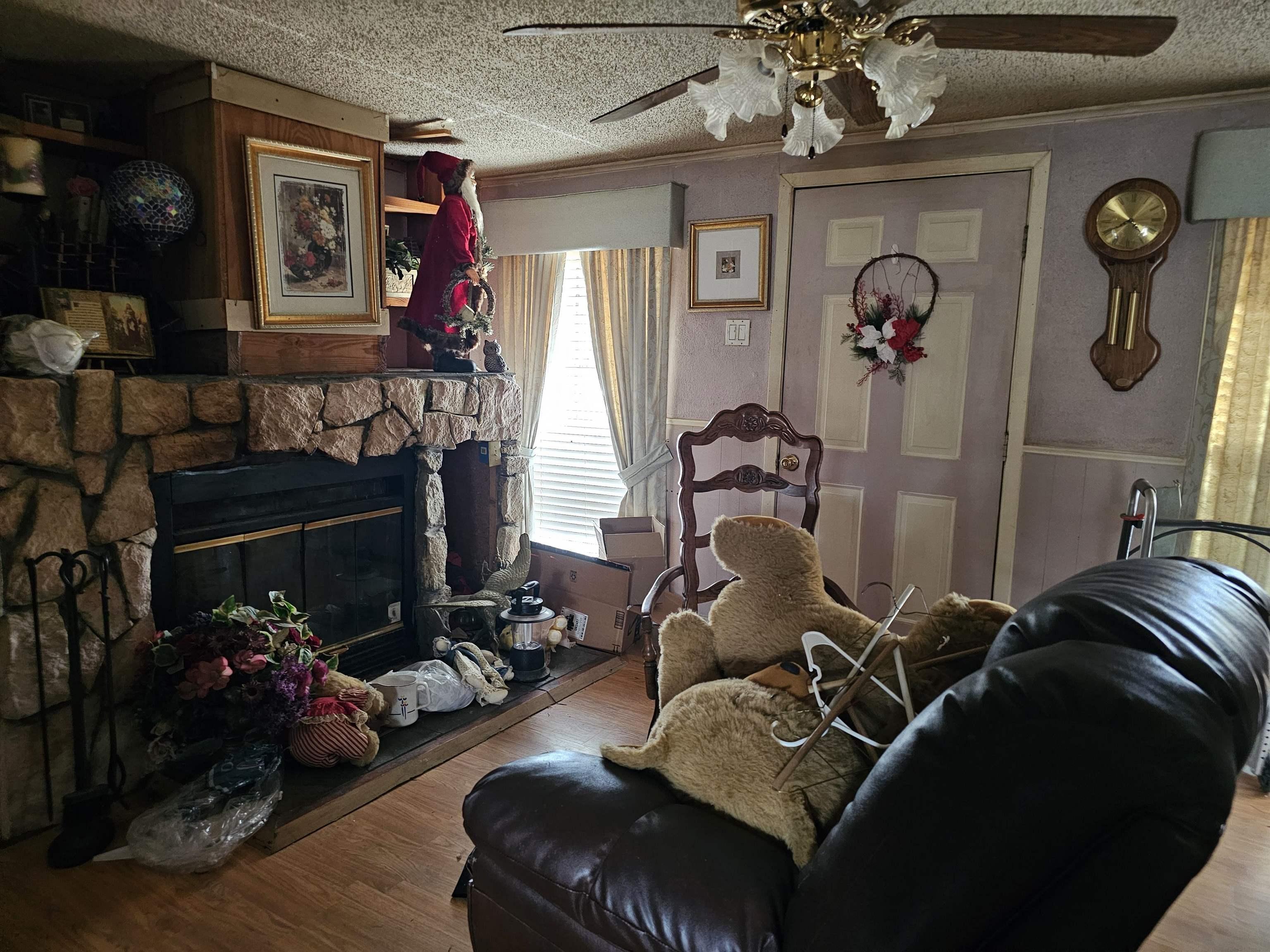 Image 0: Living room featuring a ceiling fan, a textured ceiling, wood finished floors, a stone fireplace, and wainscoting, Living Room