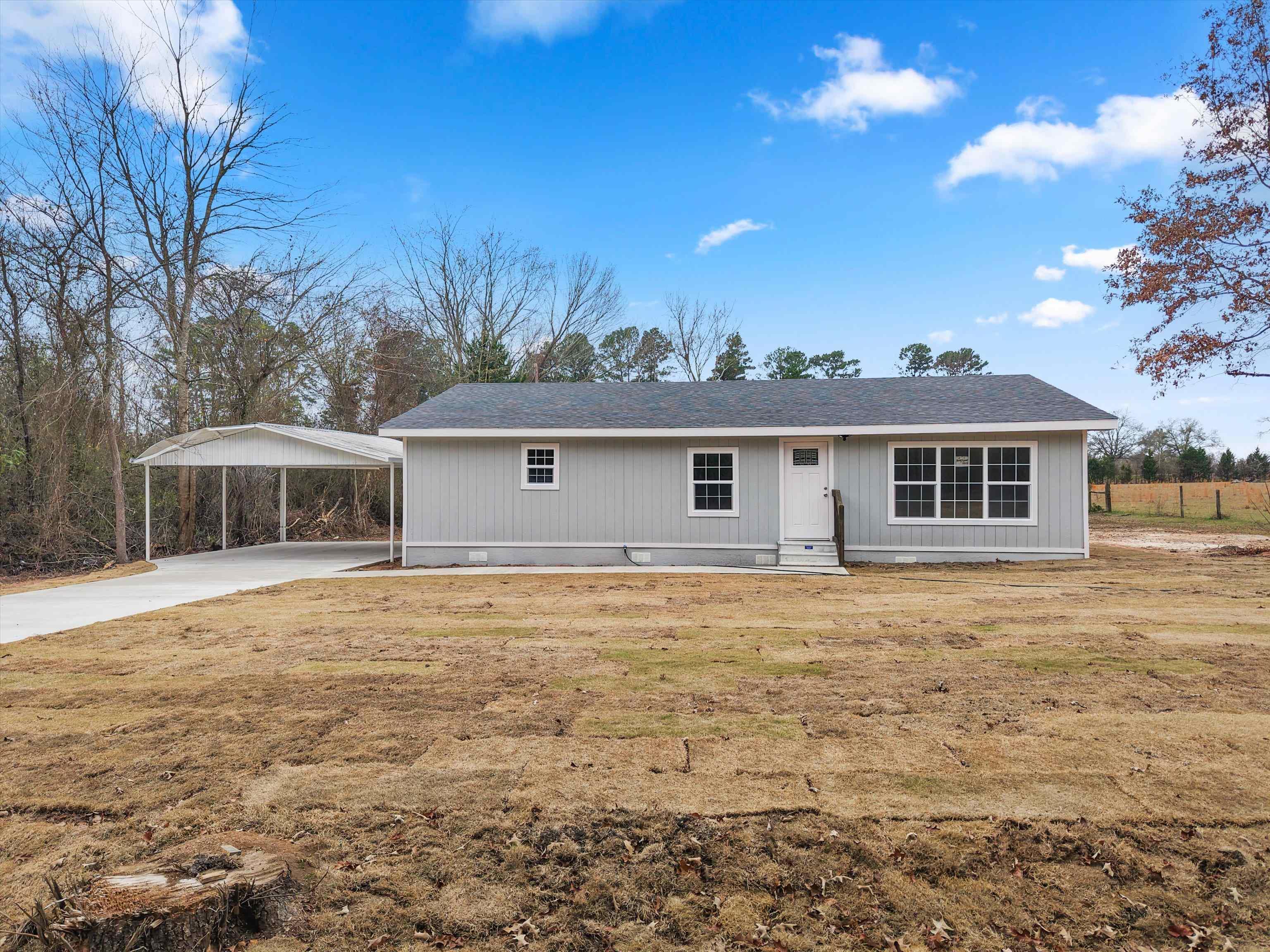 Image 1: Ranch-style house featuring a detached carport, a shingled roof, concrete driveway, and a front yard, Front Of Structure