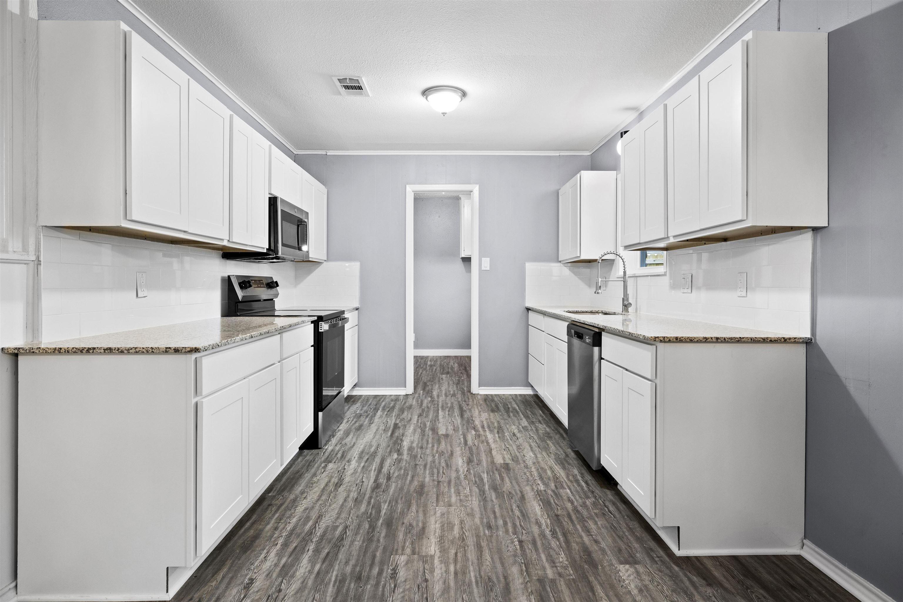 Image 1: Kitchen with stainless steel appliances, light stone countertops, white cabinetry, dark wood-style flooring, and crown molding, Kitchen