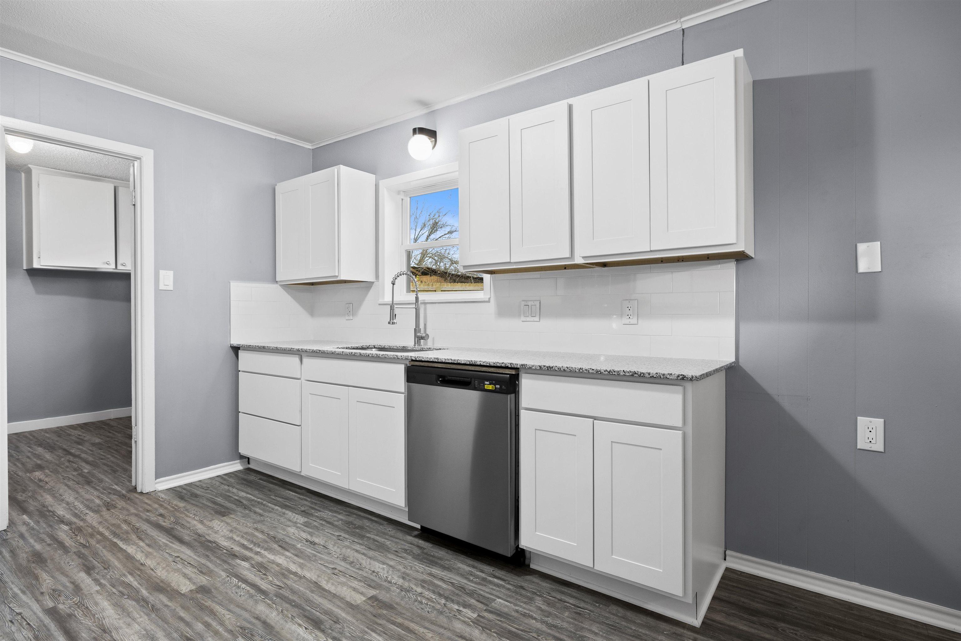 Image 3: Kitchen featuring white cabinetry, crown molding, dishwasher, light stone counters, and dark wood-type flooring, Kitchen