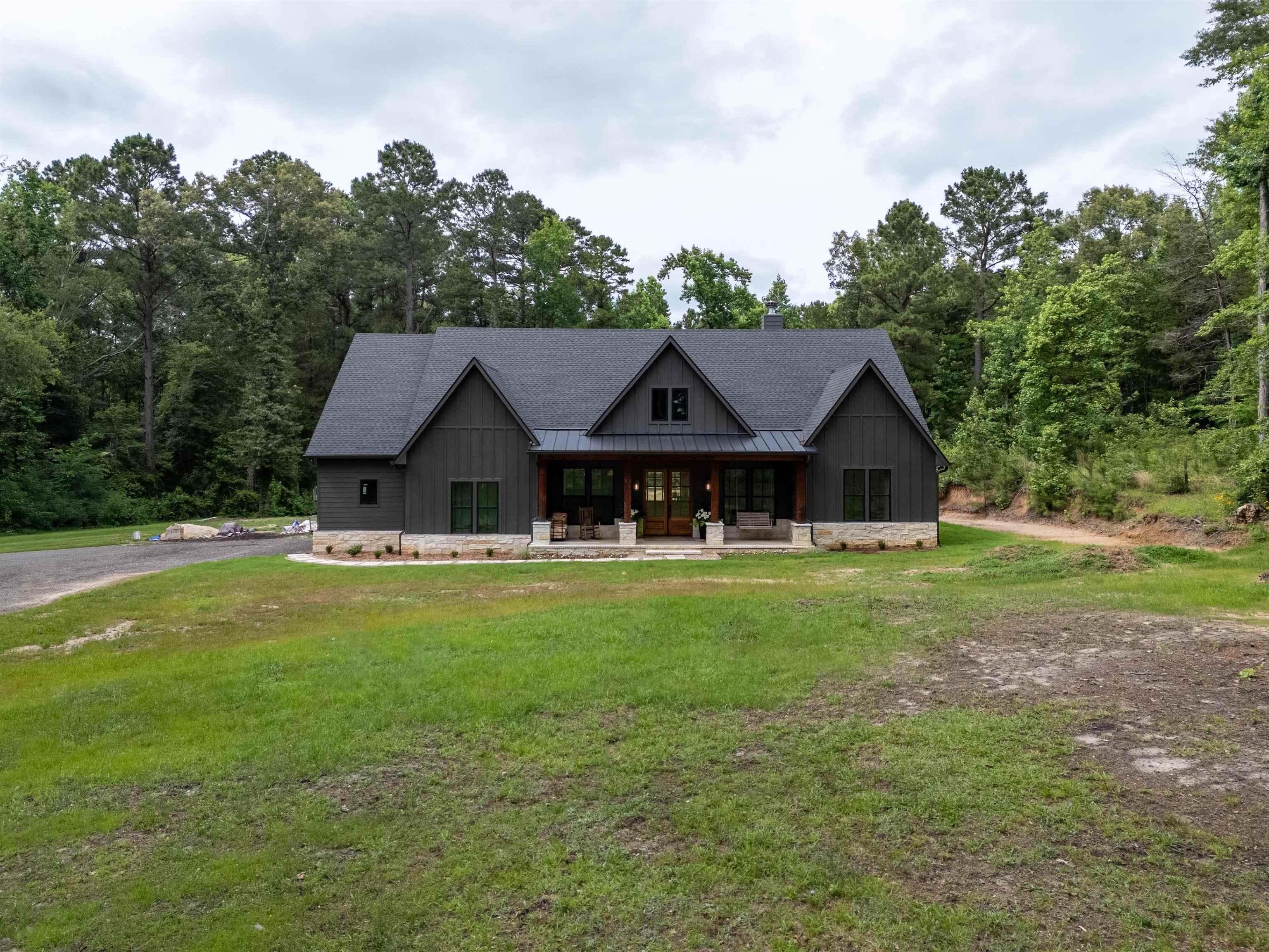 Image 2: Modern farmhouse exterior featuring dark vertical siding, a stone foundation, a covered front porch with exposed timber columns, a dark shingle roof, and multiple gables, Front Of Structure