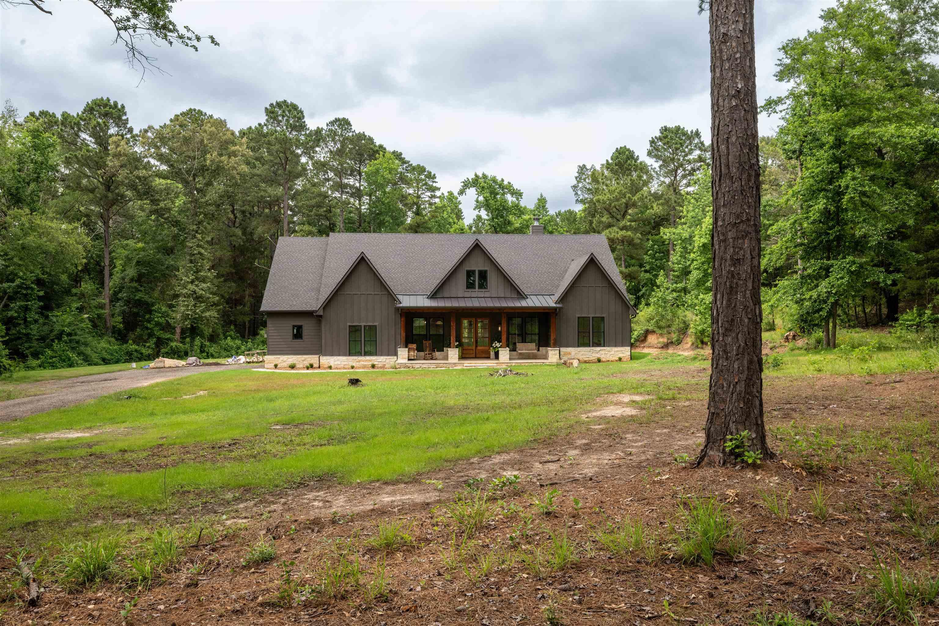 Image 3: Modern farmhouse exterior featuring board and batten siding, a prominent gable roof, stone foundation, a covered porch with timber columns, and a double entry door, Front Of Structure