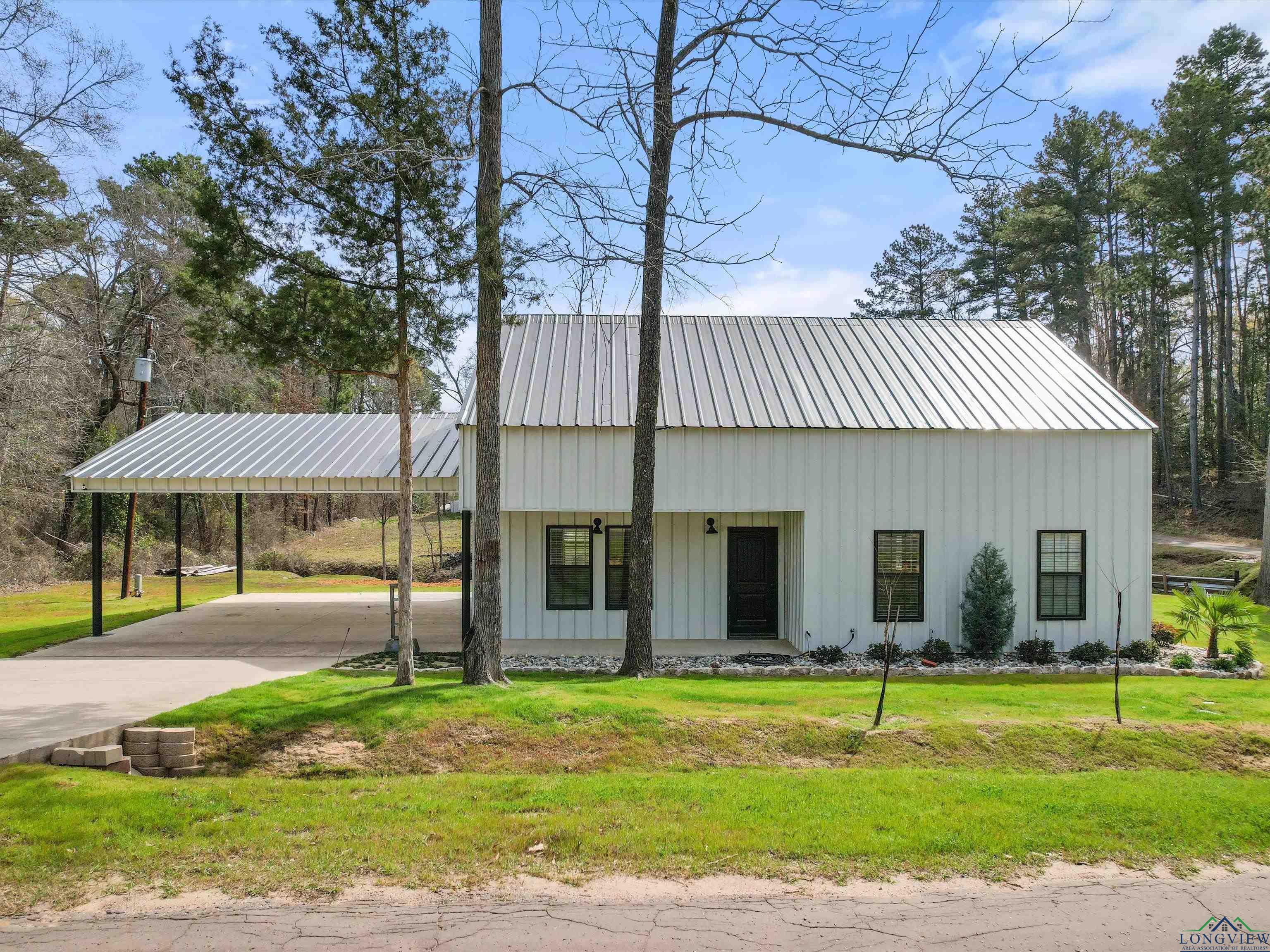 Image 0: Exterior space with metal roof, an attached carport, concrete driveway, and a front lawn, Front Of Structure