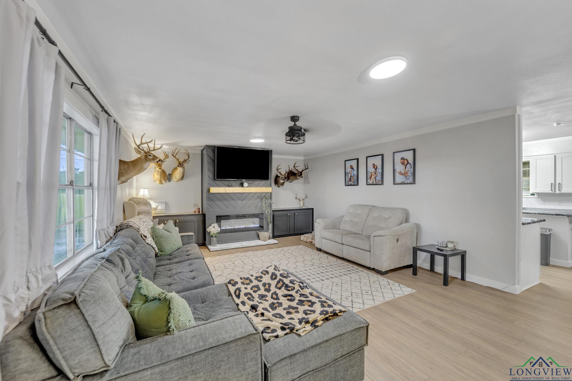 Image 5: Living area featuring a ceiling fan, a large fireplace, light wood-style floors, and ornamental molding, Living Room