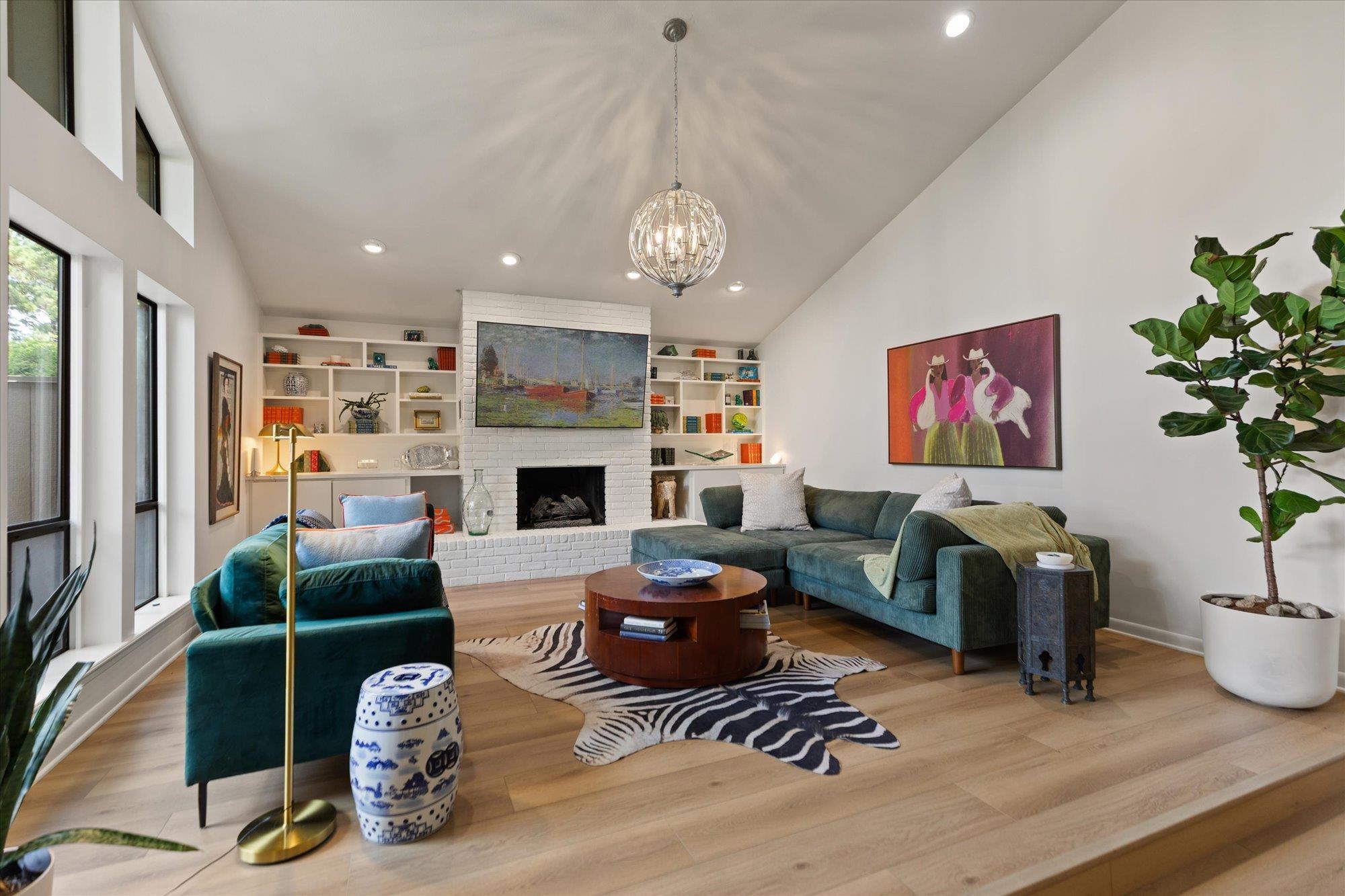 Image 2: Living area featuring vaulted ceilings, wood-finish flooring, a white brick fireplace, built-in shelving, and large windows, Living Room