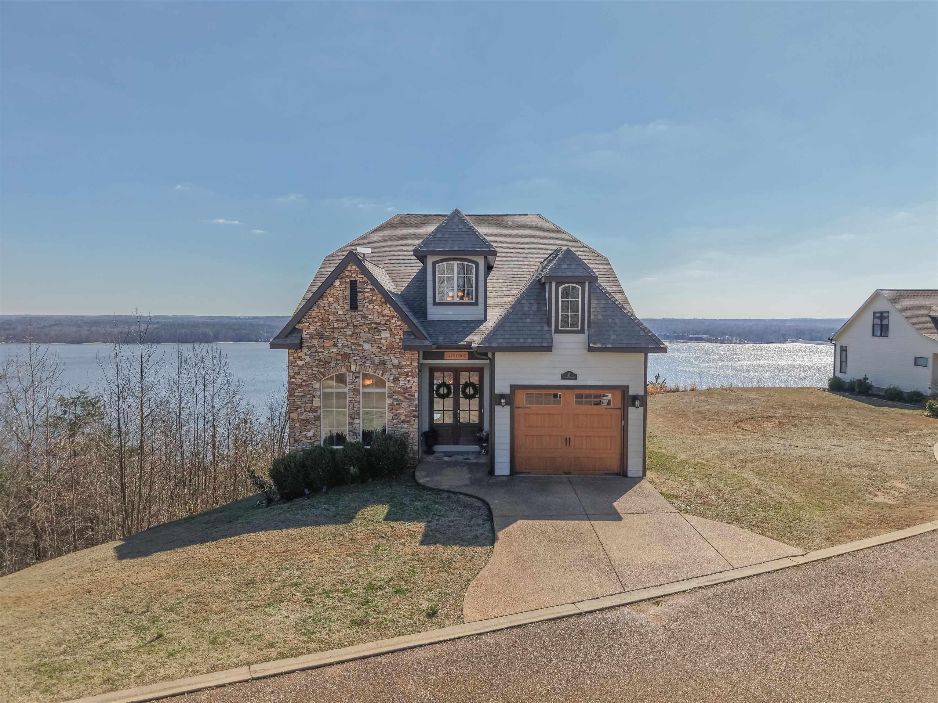 Image 1: Stone and siding exterior with a prominent dormer window, an integrated garage with a wood-finish door, and a paver driveway