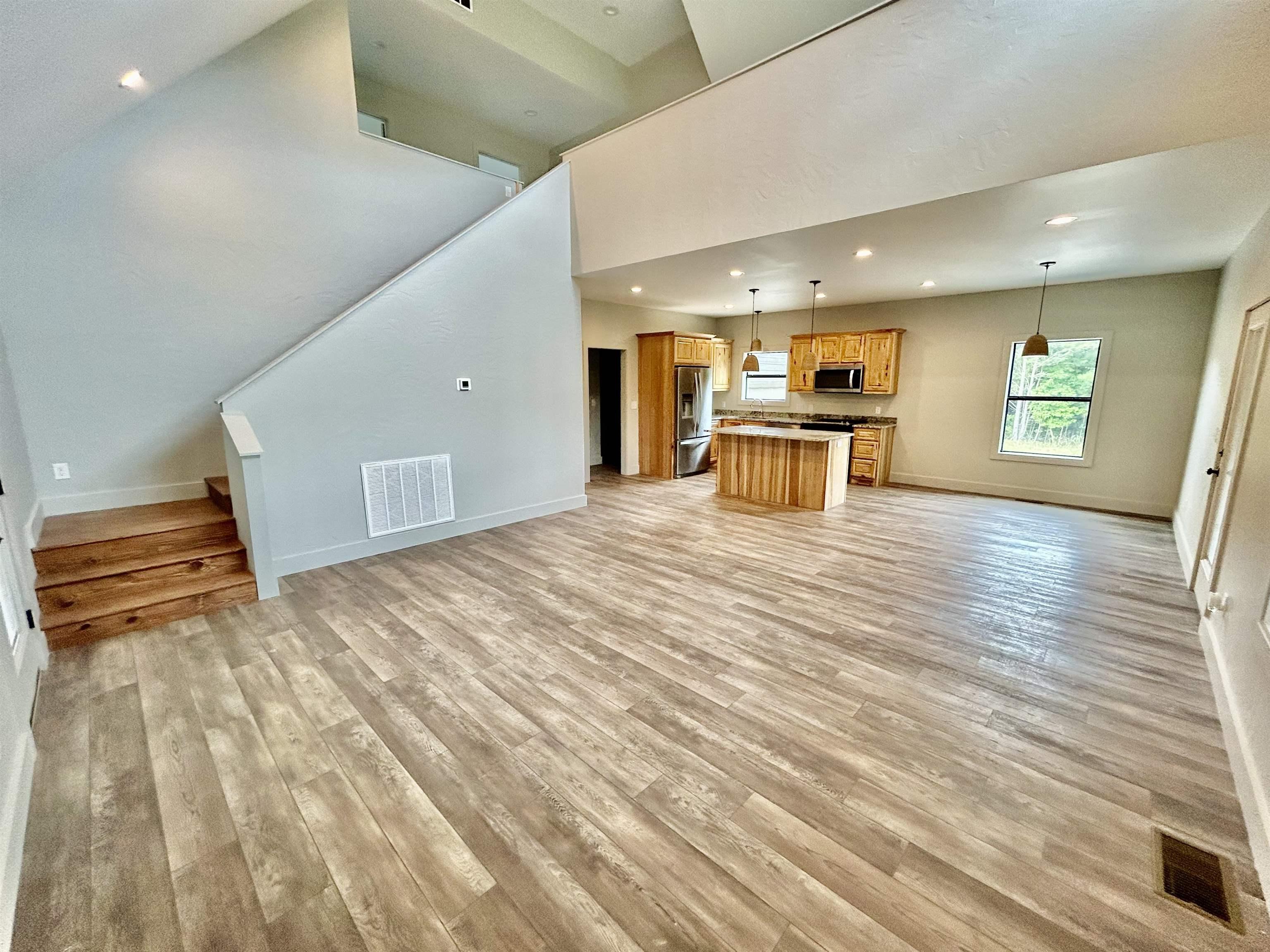 Image 3: Unfurnished living room featuring stairs, recessed lighting, light wood finished floors, and a towering ceiling