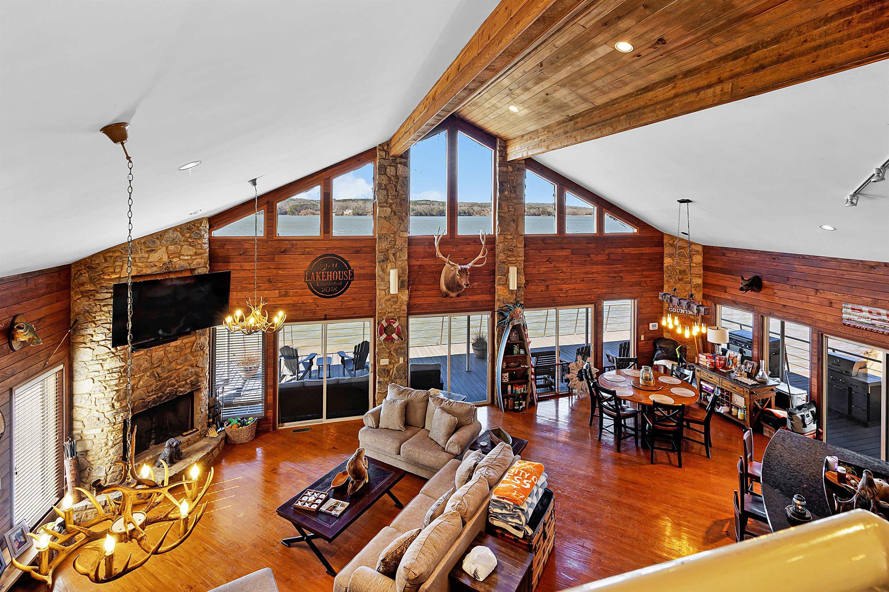 Image 3: Living room featuring wood walls, a notable chandelier, a stone fireplace, and wood finished floors