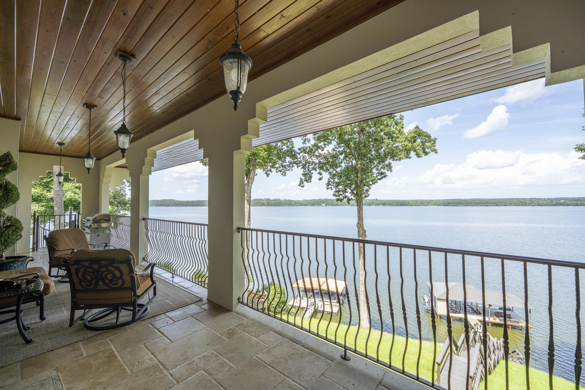 Image 2: Expansive covered patio featuring a wood-finish ceiling, decorative pendant lighting, and a wrought iron railing overlooking the lake