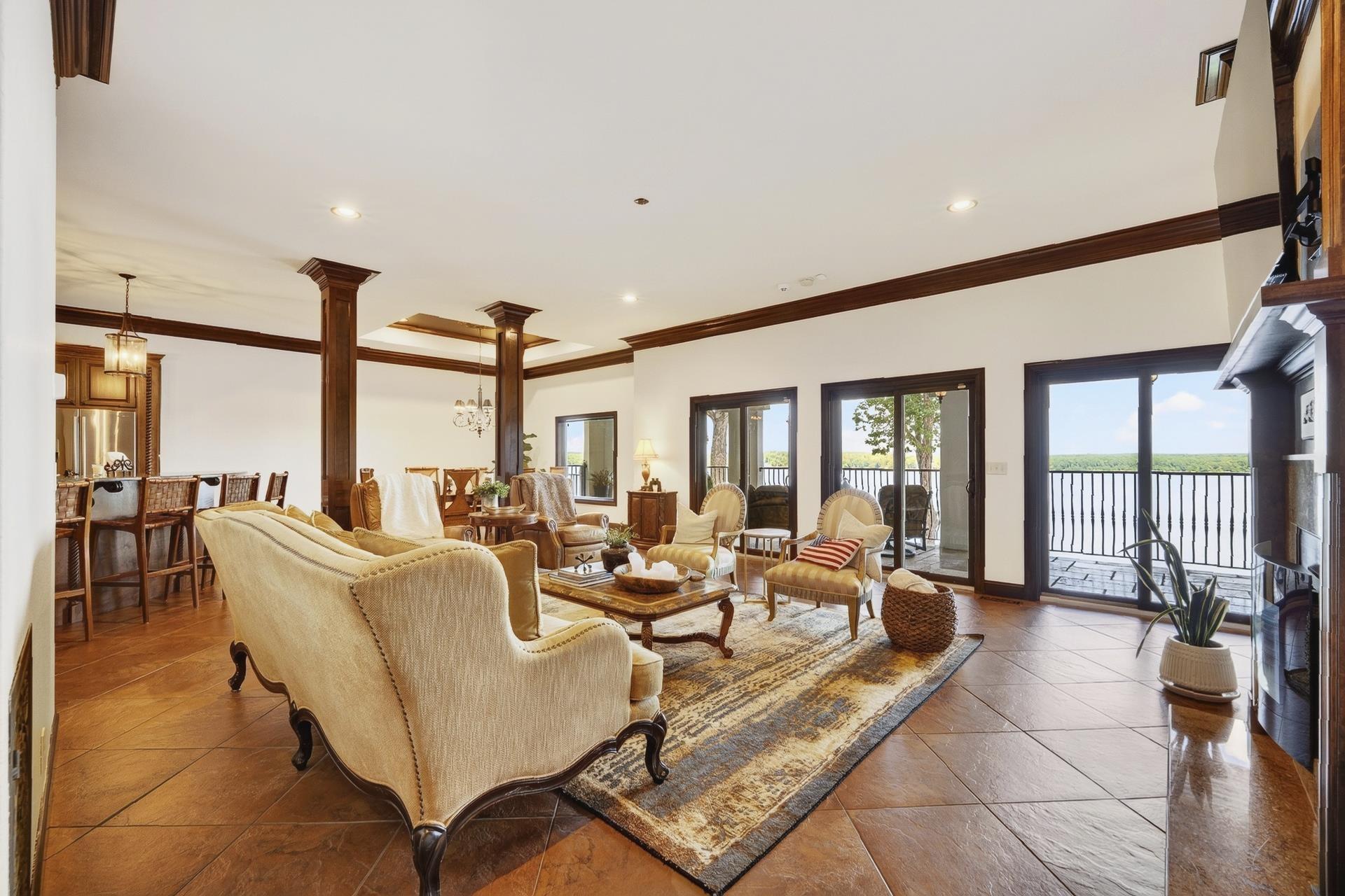 Image 4: Spacious living area featuring large sliding glass doors opening to a balcony, a prominent fireplace with a substantial mantel, rich wood-finish trim and columns, and large format tile flooring