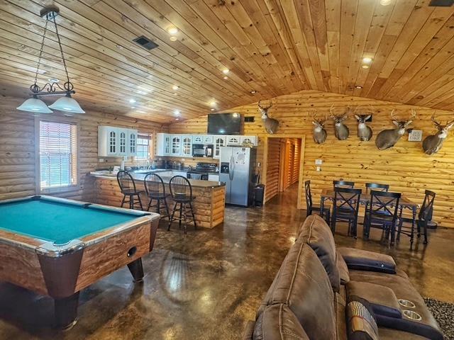 Image 4: Rec room with rustic walls, billiards table, finished concrete flooring, a vaulted wooden ceiling, and recessed lighting