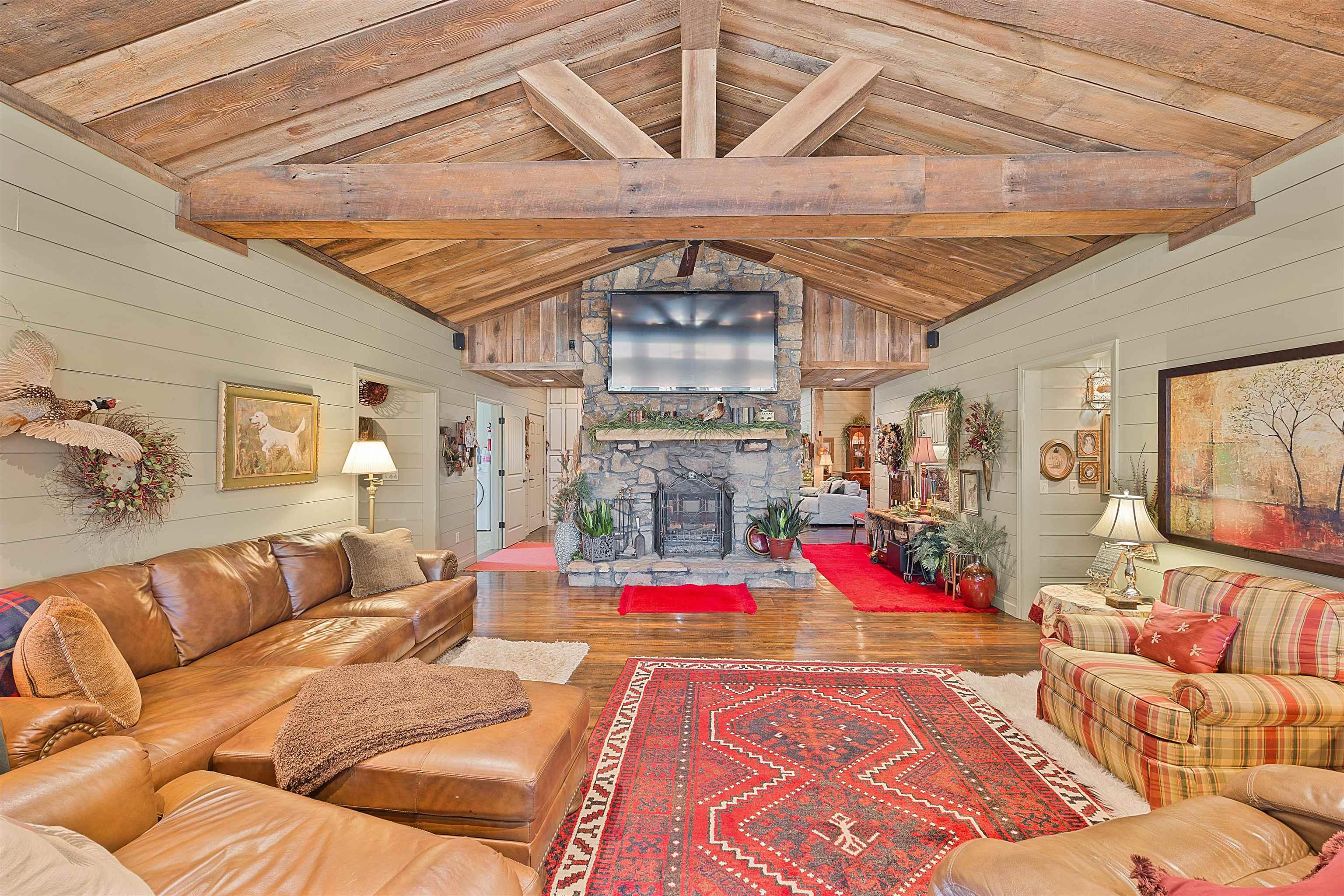 Image 4: Living room with vaulted ceiling with beams, wood ceiling, wood walls, wood-type flooring, and a fireplace