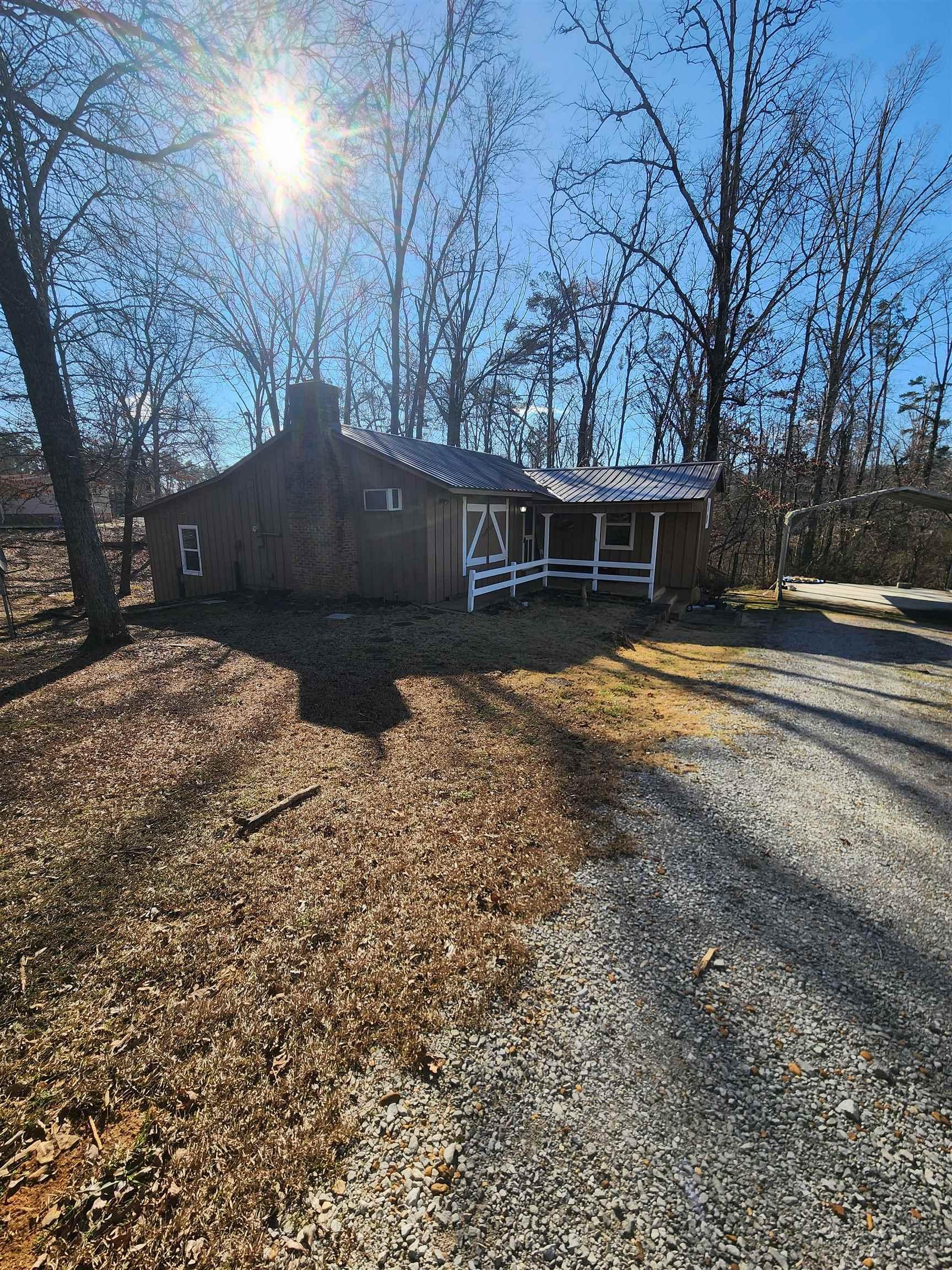 Image 1: View of front facade featuring a metal roof, gravel driveway, a detached carport, and a chimney
