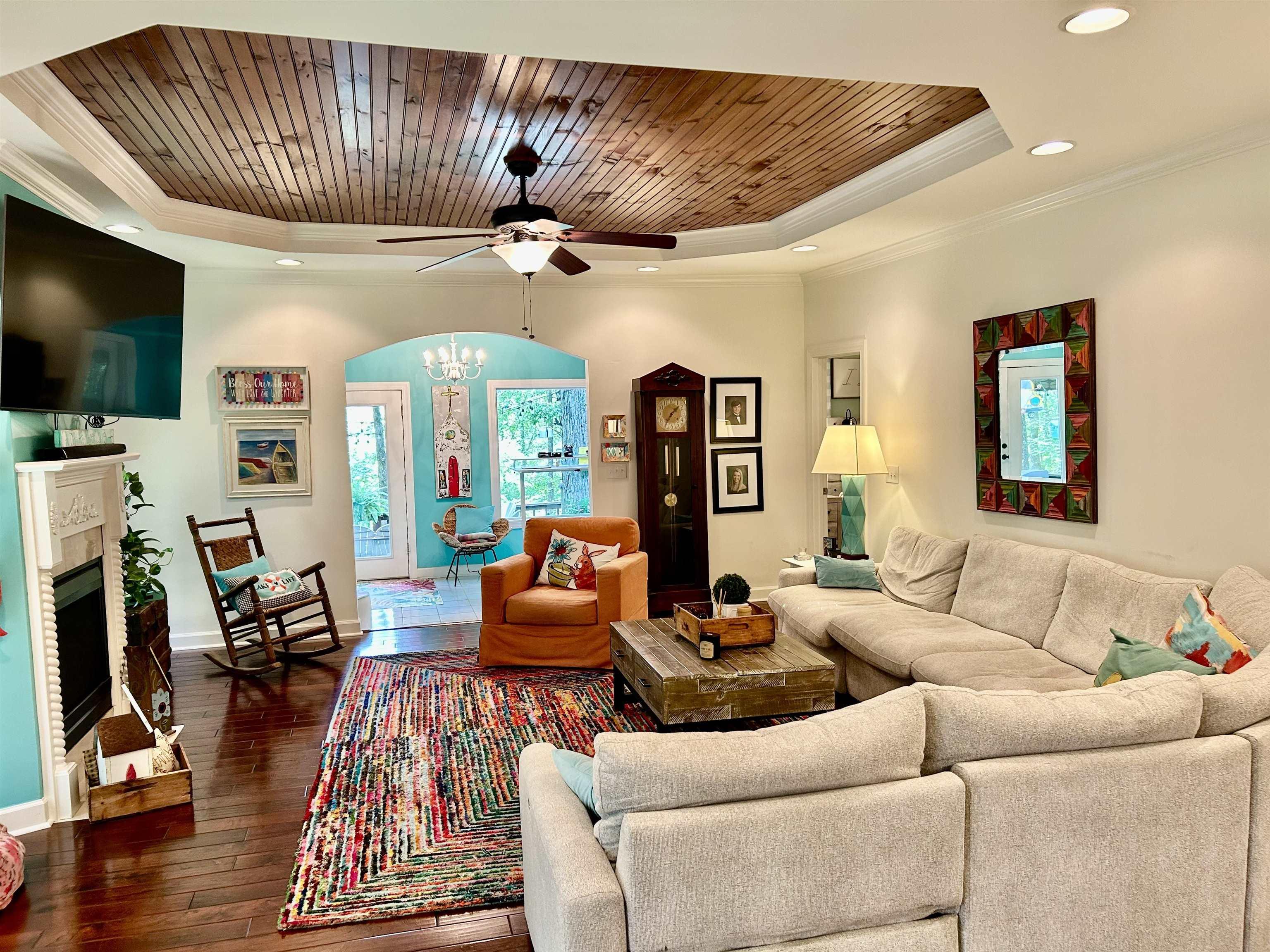 Image 4: Living area with a tray ceiling, ornamental molding, dark wood-style floors, a ceiling fan, and a chandelier