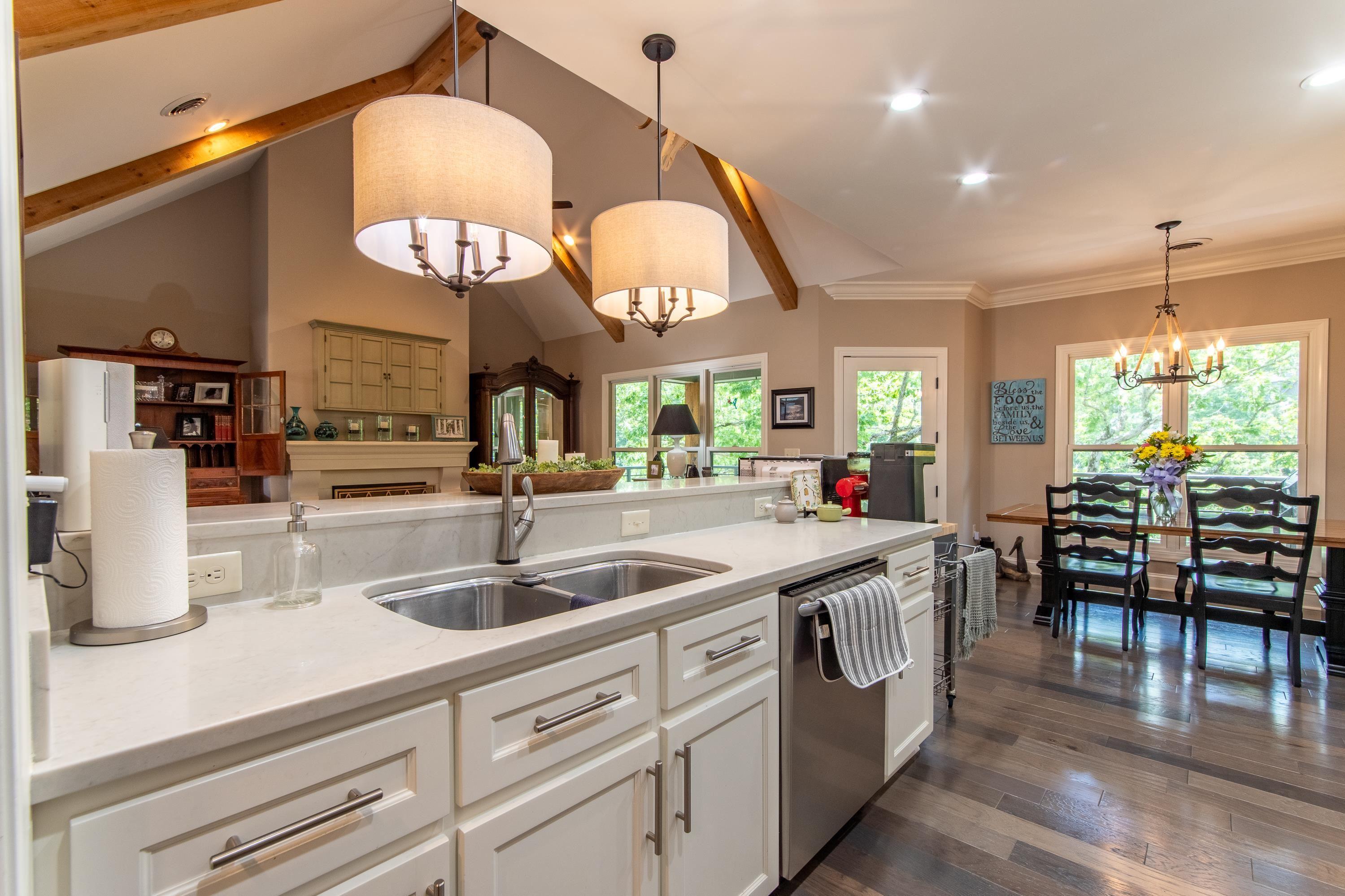 Image 2: Kitchen with decorative light fixtures, stainless steel dishwasher, white cabinetry, vaulted ceiling with beams, and dark hardwood / wood-style floors