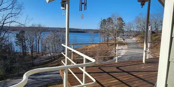Image 3: Expansive wood-finish deck with white metal railings, offering serene water and tree-lined shoreline