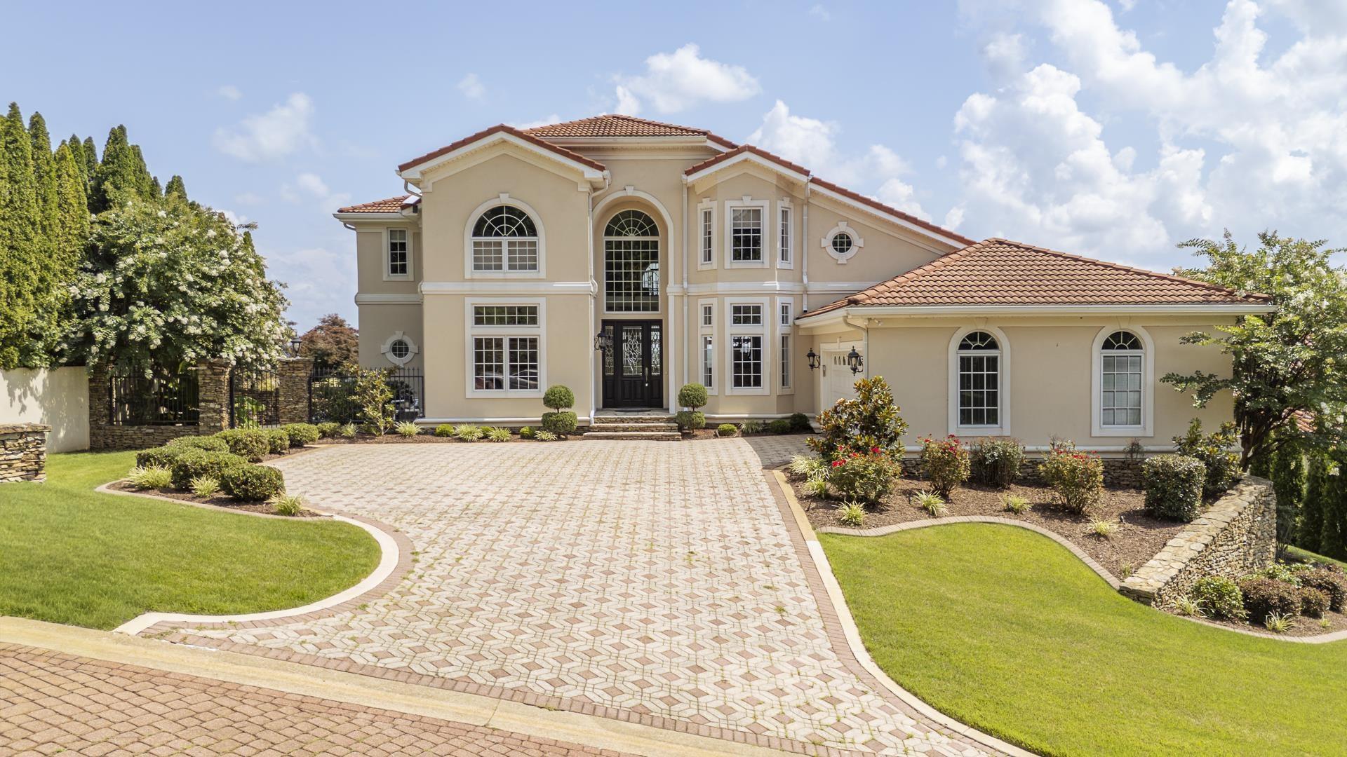 Image 1: Stucco exterior with a terracotta tile roof, prominent arched windows, a multi-level paver driveway, and landscaped grounds featuring mature trees and shrubbery