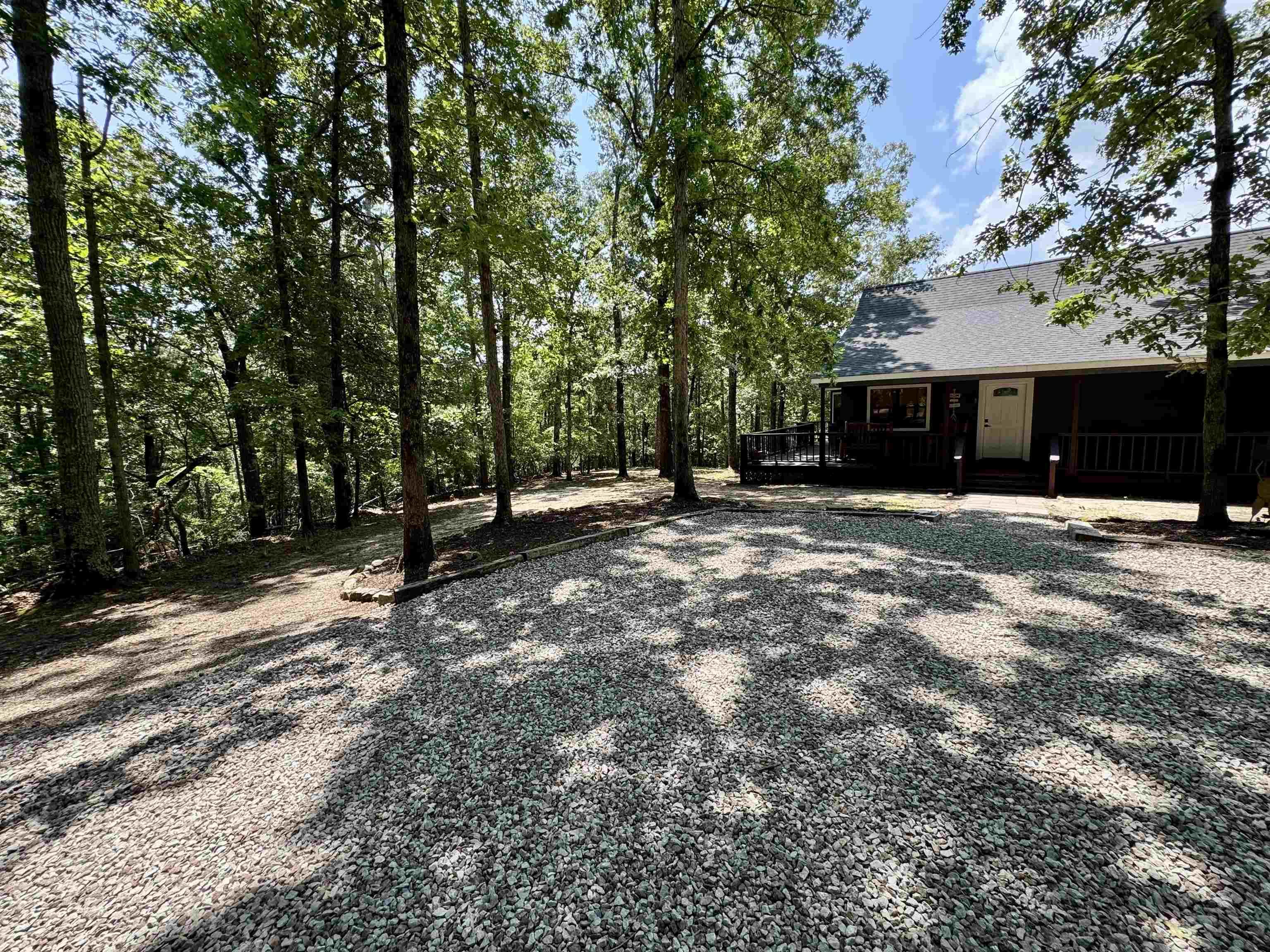 Image 2: Wooded lot with gravel driveway, dark-stained exterior, and covered porch with railing