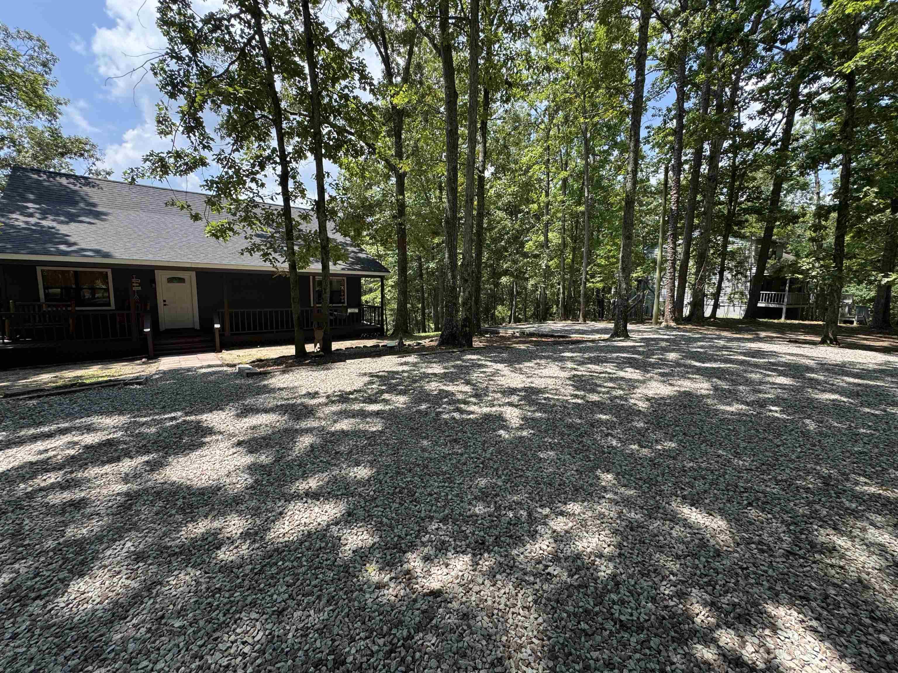 Image 3: Gravel driveway with extensive tree coverage and a single-story residence featuring a covered porch