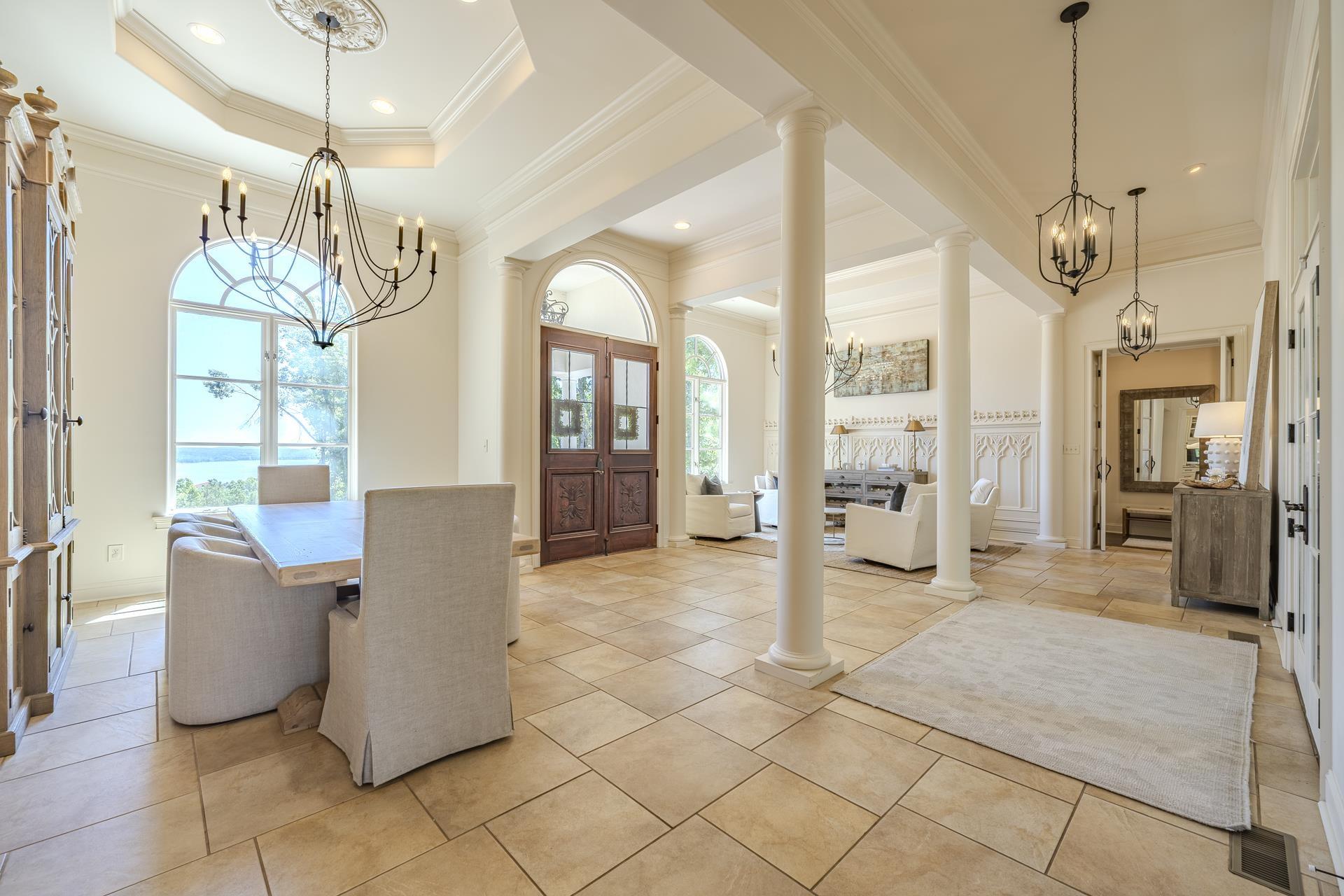 Image 4: Spacious open-concept interior featuring light-toned large format tile flooring, multiple arched windows, prominent structural columns, and a double-entry carved wood door