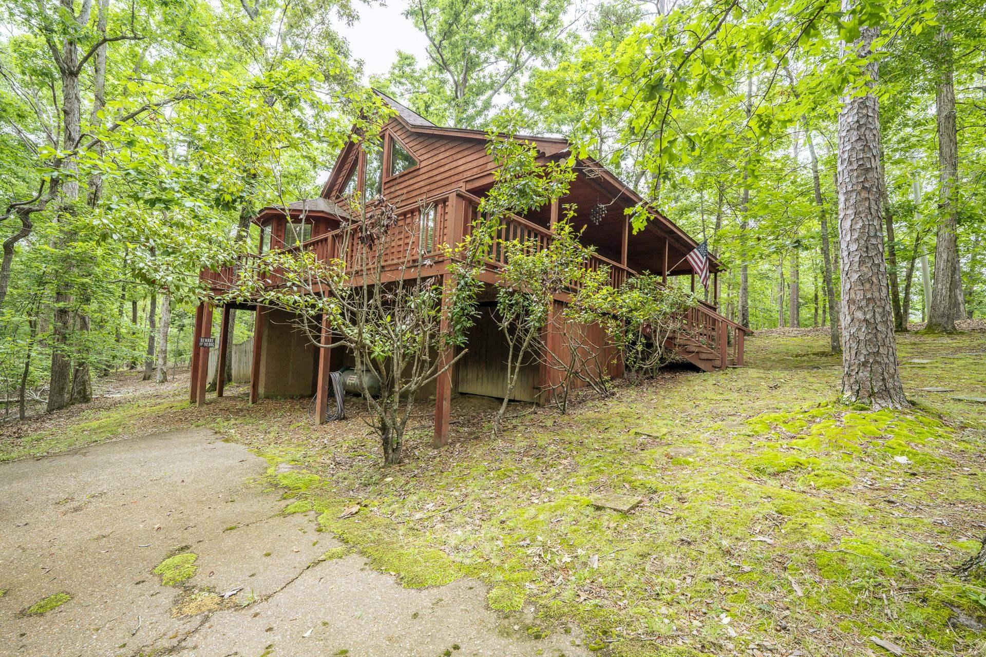 Image 2: Raised wooden structure featuring a wraparound deck, natural wood siding, and mature trees