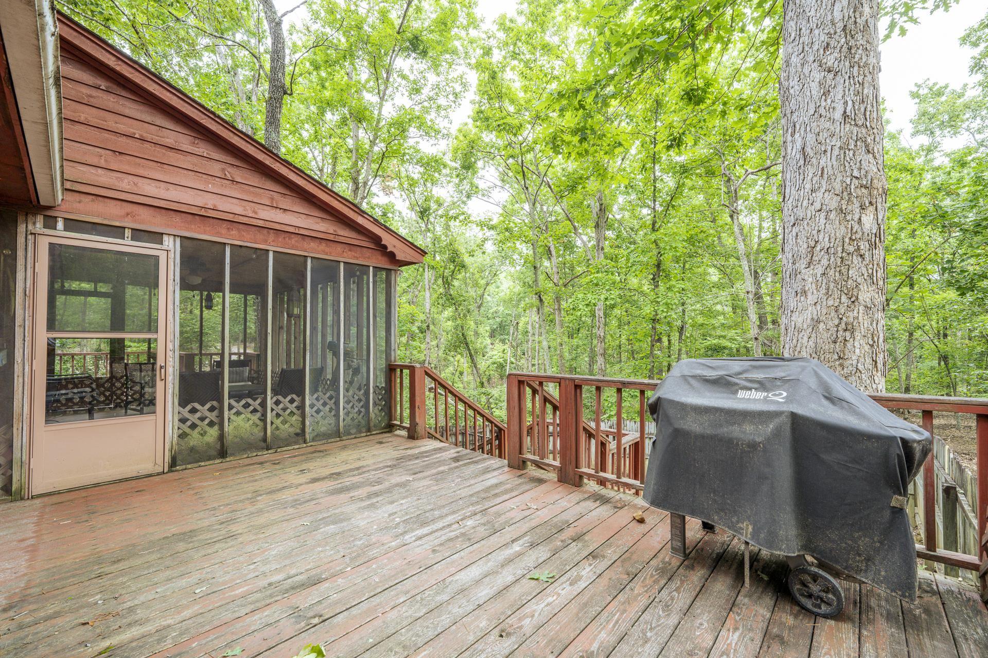 Image 4: Spacious outdoor deck with wood flooring and red railings, featuring an attached screened porch with wood siding