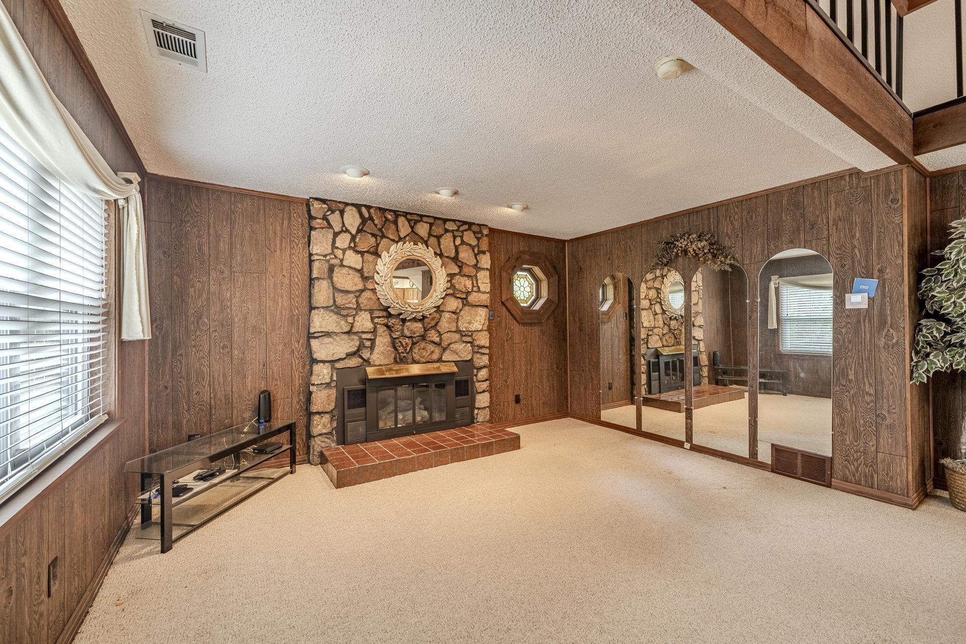Image 3: Stone-clad fireplace with a raised brick hearth, recessed ceiling lights, wood-finish wall paneling, and built-in arched mirrors