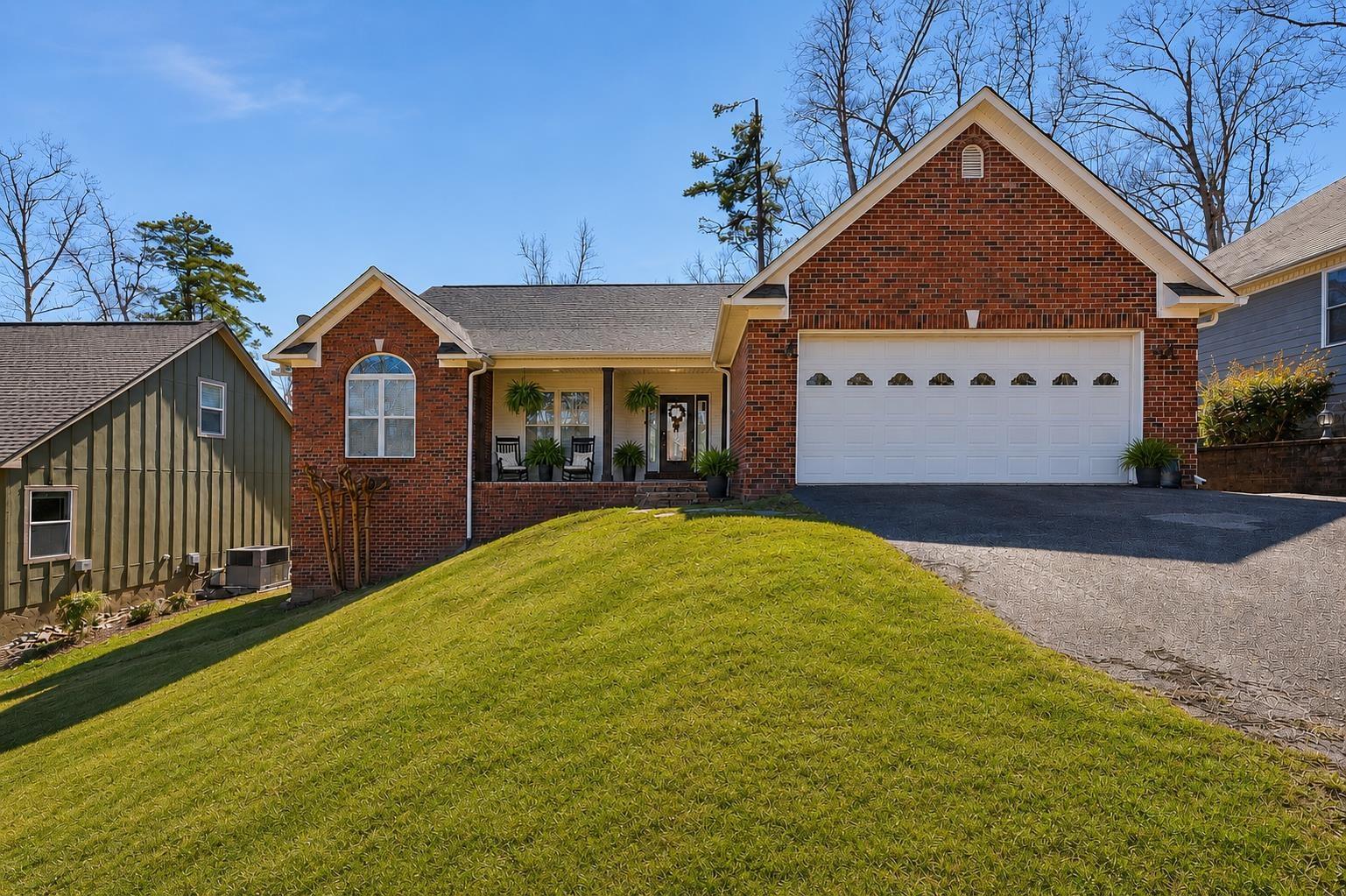 Image 4: Brick front residence with a covered porch, an attached garage, and a steeply sloped front lawn