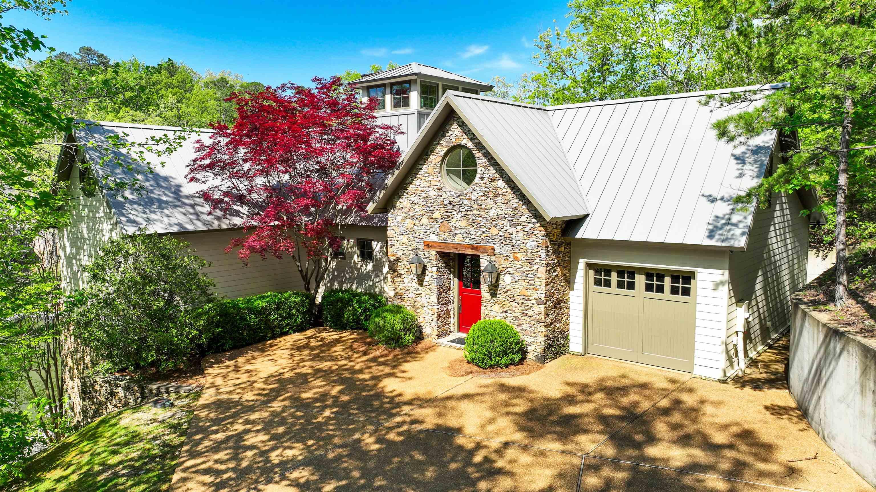 Image 2: View of front facade with stone siding, a standing seam roof, driveway, and metal roof