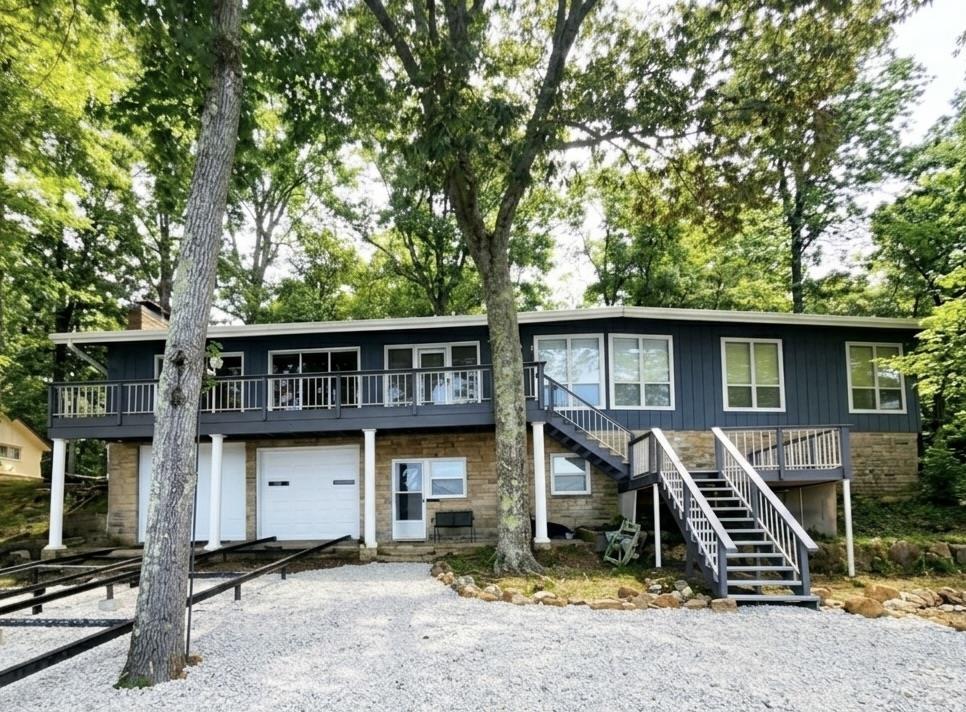 Image 1: View of front facade with a garage, gravel driveway, a deck, stone siding, and a patio