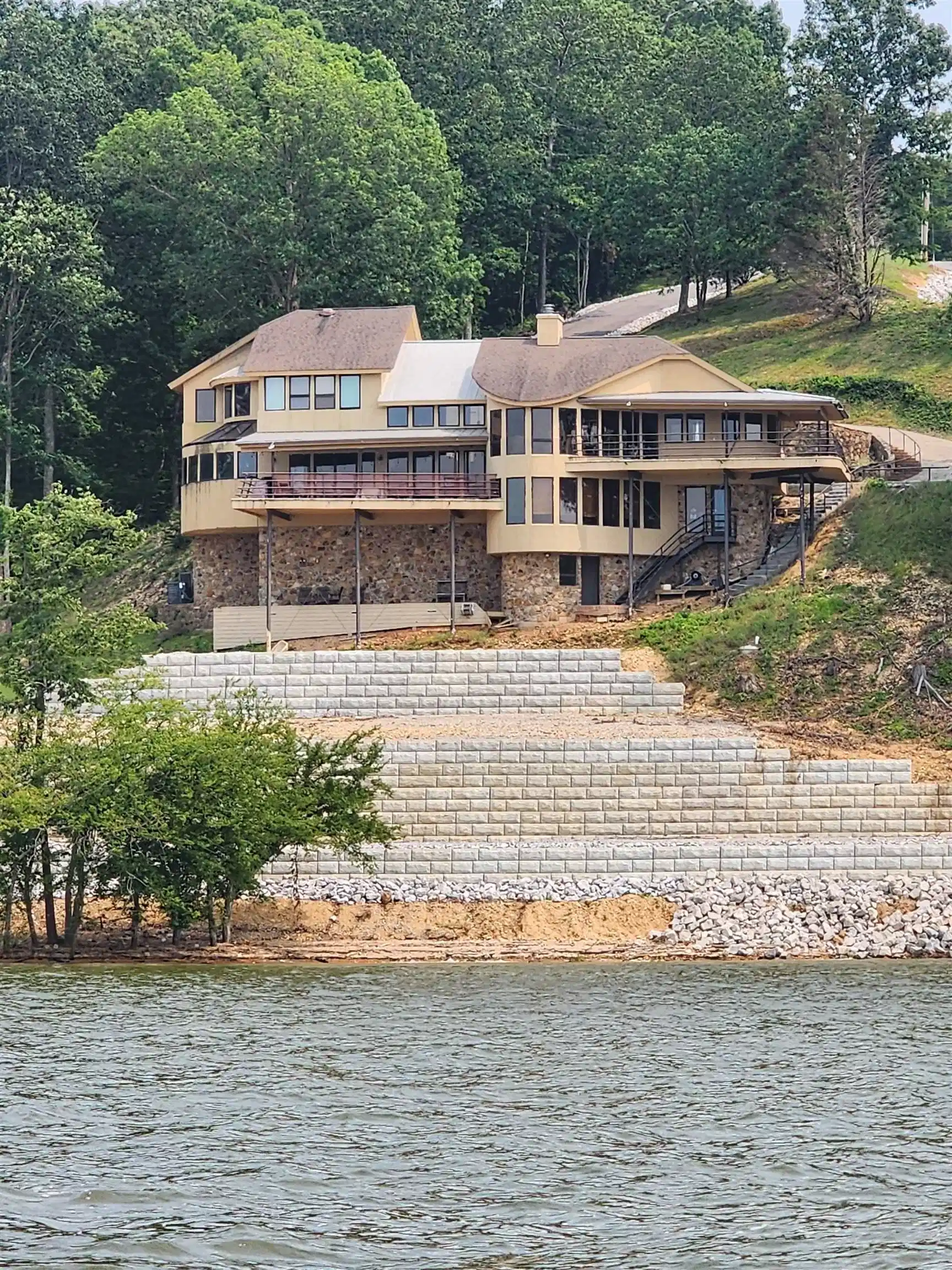 Image 1: Back of property featuring a chimney, a deck with water view, and stone siding