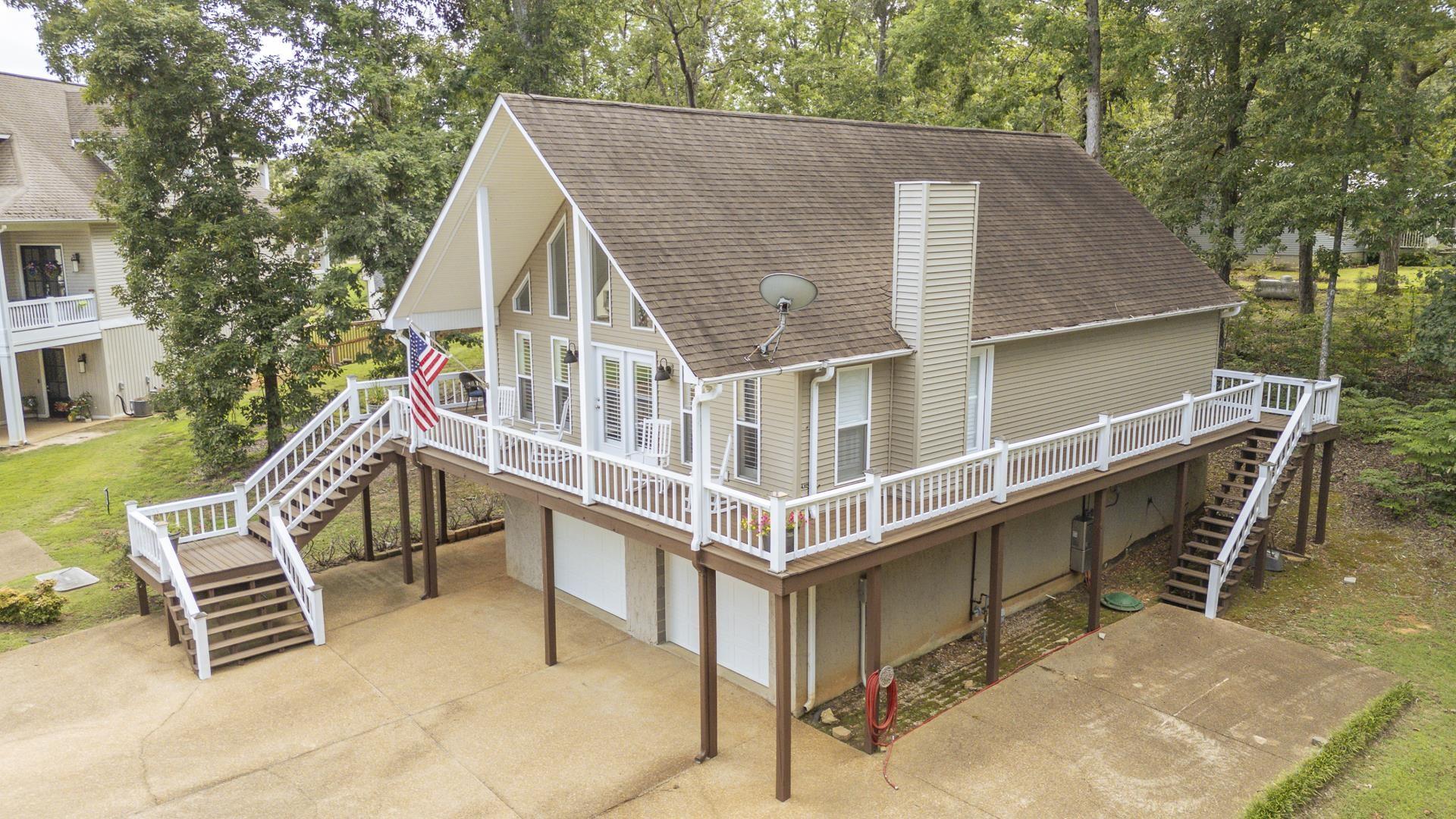 Image 2: Raised A-frame residence featuring an expansive wrap-around deck with white railings, a prominent main-level chimney, and a full-height window wall on the front facade