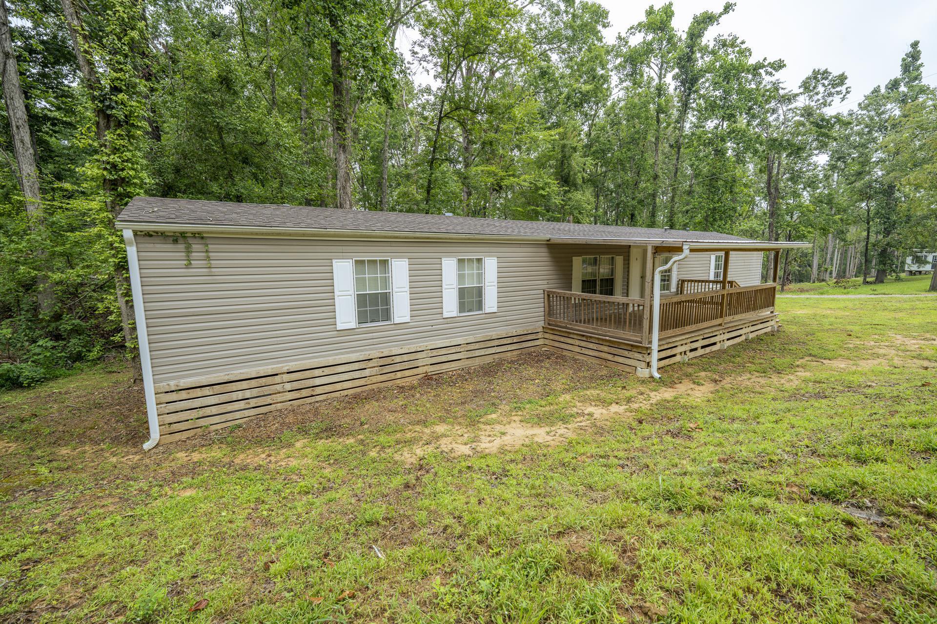 Image 2: Single-story residence featuring light-toned horizontal siding, white window shutters, a covered porch, and a wooden deck with a ramp